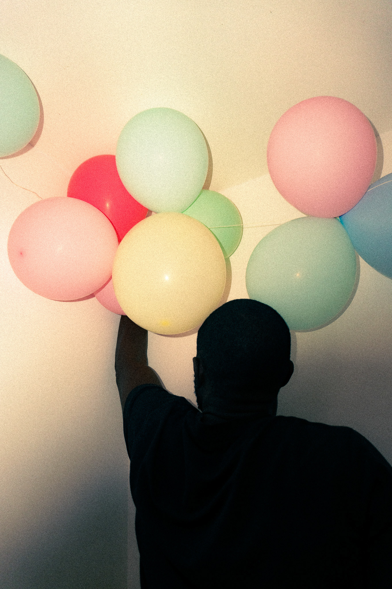 A black man sets up baloons for a party in pastels tones