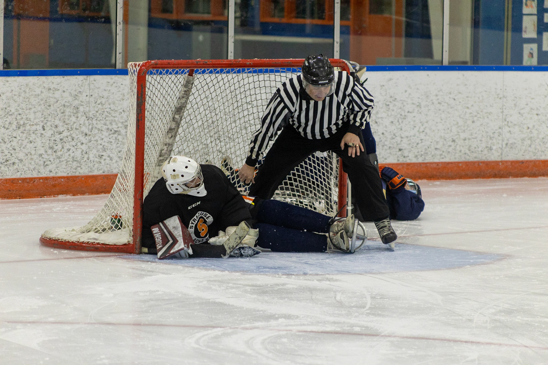 The CNY Flyers, a sled hockey team, played against the Syracuse University Men's Club Hockey team on 11/19/22 at Tennity Ice Skating Pavilion. The game ended with the Flyers scoring 8 to Syracuse 0 with 25 shots on goal by the Flyers compared to Syracuse's 2. While the game was still competitive, it was more for the fun of the sport with smiles shared by all. It was also a new experience for the Syracuse team which consisted of able-bodied individuals who may have never experienced sled hockey. Referee, Garth Werner, recovers the puck after a flyers goal against Syracuse.