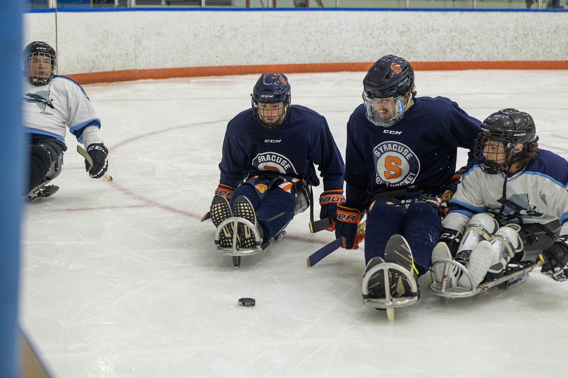 The CNY Flyers, a sled hockey team, played against the Syracuse University Men's Club Hockey team on 11/19/22 at Tennity Ice Skating Pavilion. The game ended with the Flyers scoring 8 to Syracuse 0 with 25 shots on goal by the Flyers compared to Syracuse's 2. While the game was still competitive, it was more for the fun of the sport with smiles shared by all. It was also a new experience for the Syracuse team which consisted of able-bodied individuals who may have never experienced sled hockey. Syracuse and Flyers players push to reach the puck before the other can take possession.