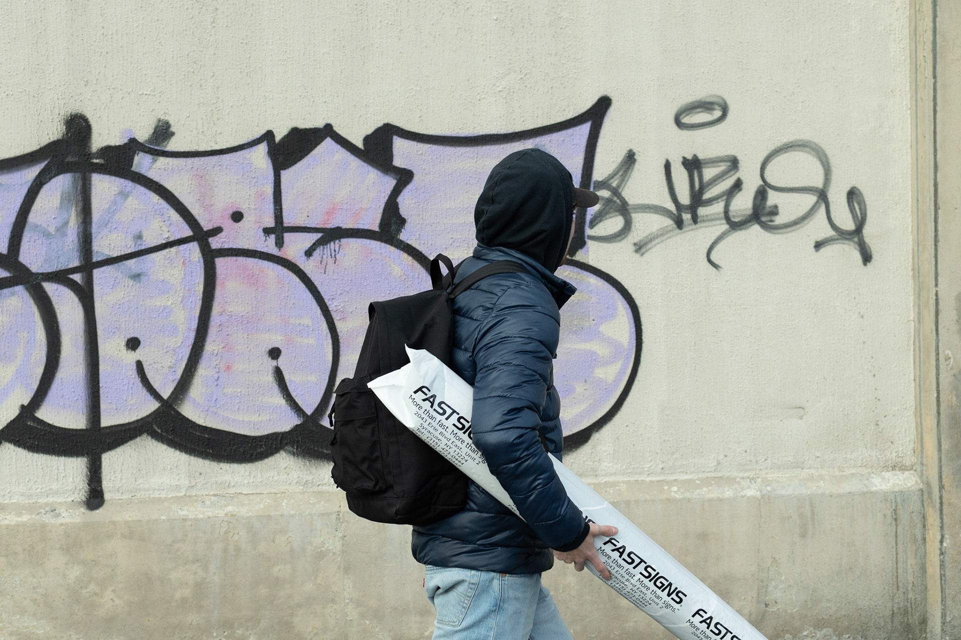 Jacob Wilkes prepares and hangs a wall art decal on the outside of the Old Abandoned Train Platform Station for his project of street art around Syracuse. Taken on 02/20/22.