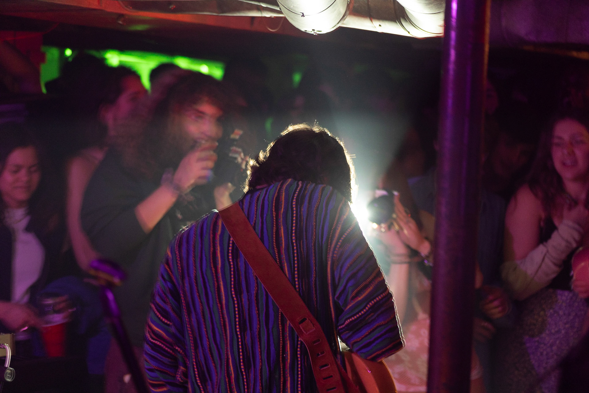 Maddi Brown takes pictures at a  concert  hosted by The Harrison, a student run music venue hosted in the basement of a Sumner residence. Images taken the night of 3/04/22. The bass player of the band is illimuniate by another flash as Maddi lines up the shot to capture the main singer of the band, a friend of hers.