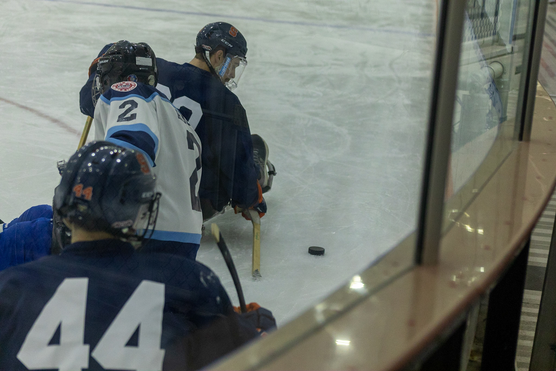 The CNY Flyers, a sled hockey team, played against the Syracuse University Men's Club Hockey team on 11/19/22 at Tennity Ice Skating Pavilion. The game ended with the Flyers scoring 8 to Syracuse 0 with 25 shots on goal by the Flyers compared to Syracuse's 2. While the game was still competitive, it was more for the fun of the sport with smiles shared by all. It was also a new experience for the Syracuse team which consisted of able-bodied individuals who may have never experienced sled hockey. Syracuse and Flyers players pile up as they compete for possession of the puck.