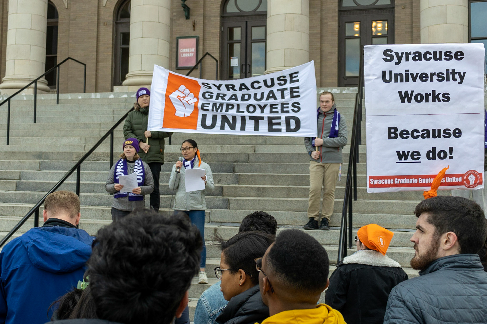 The Syracuse Graduate Employees Union gathered fellow students, supporting faculty and staff, as well as regular observers at the steps of Carnegie Library as they advocated for the University to recognize the union and accept the union's demands. The group then marched to the student center and onwards to the administration building where leaders would meet with the Provost.