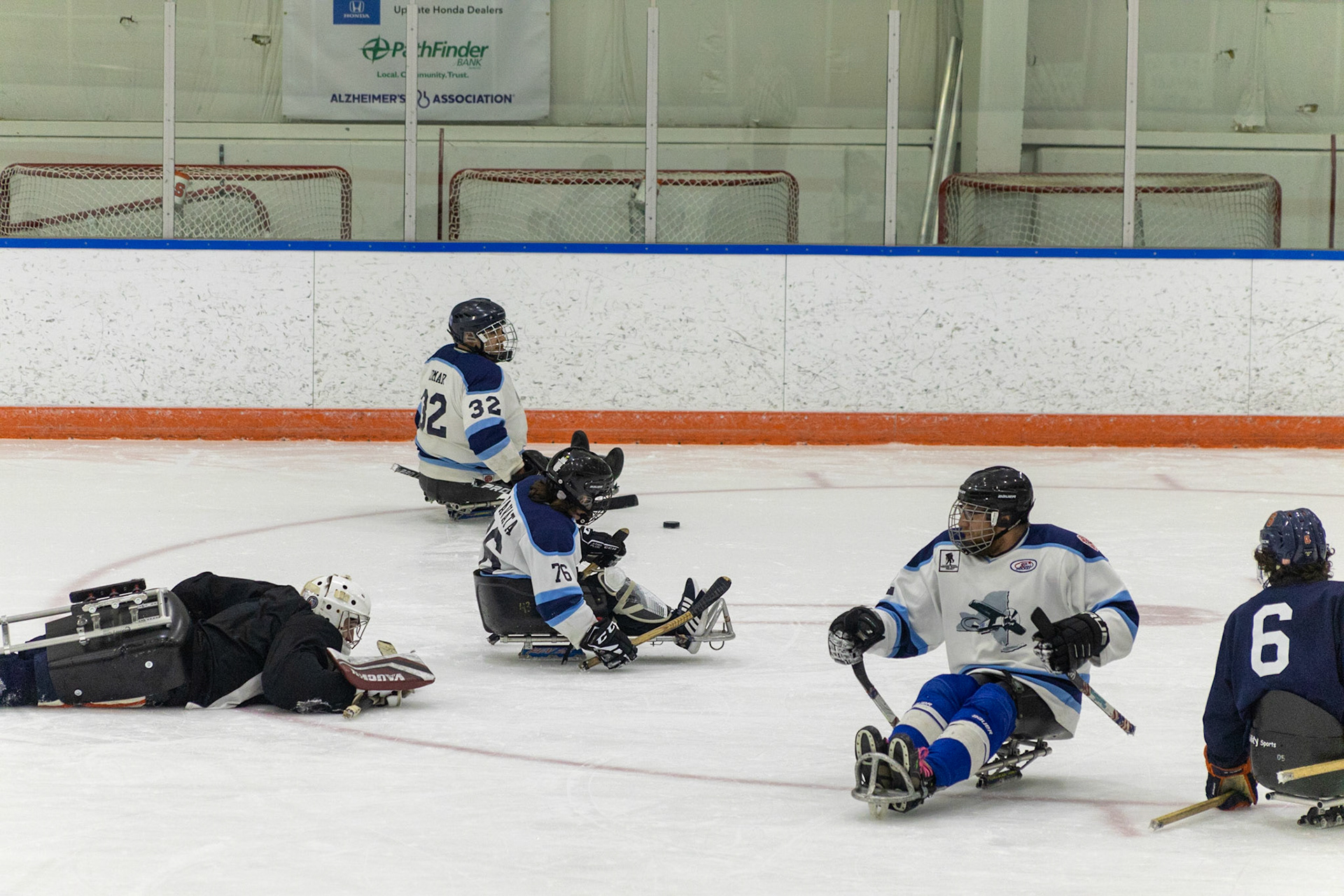 The CNY Flyers, a sled hockey team, played against the Syracuse University Men's Club Hockey team on 11/19/22 at Tennity Ice Skating Pavilion. The game ended with the Flyers scoring 8 to Syracuse 0 with 25 shots on goal by the Flyers compared to Syracuse's 2. While the game was still competitive, it was more for the fun of the sport with smiles shared by all. It was also a new experience for the Syracuse team which consisted of able-bodied individuals who may have never experienced sled hockey. The Syracuse goalie lies flat on the ice after making a risky play moving forwards resulting in the Flyers moving past with little resistance.