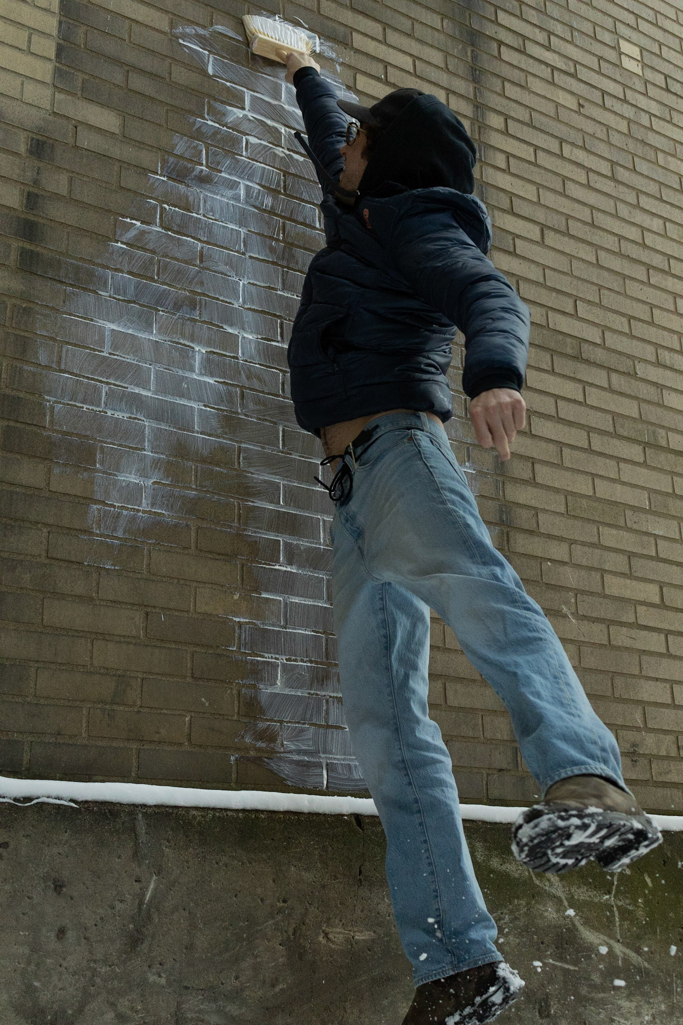 Jacob Wilkes prepares and hangs a wall art decal on the outside of the Old Abandoned Train Platform Station for his project of street art around Syracuse. Taken on 02/20/22. The walls behind the smoke stack at the Old Abandoned Train Station lend themselves perfectly to Jacob Wilkes project, so he jumps to paint the glue on the wall which he will stick his art to.