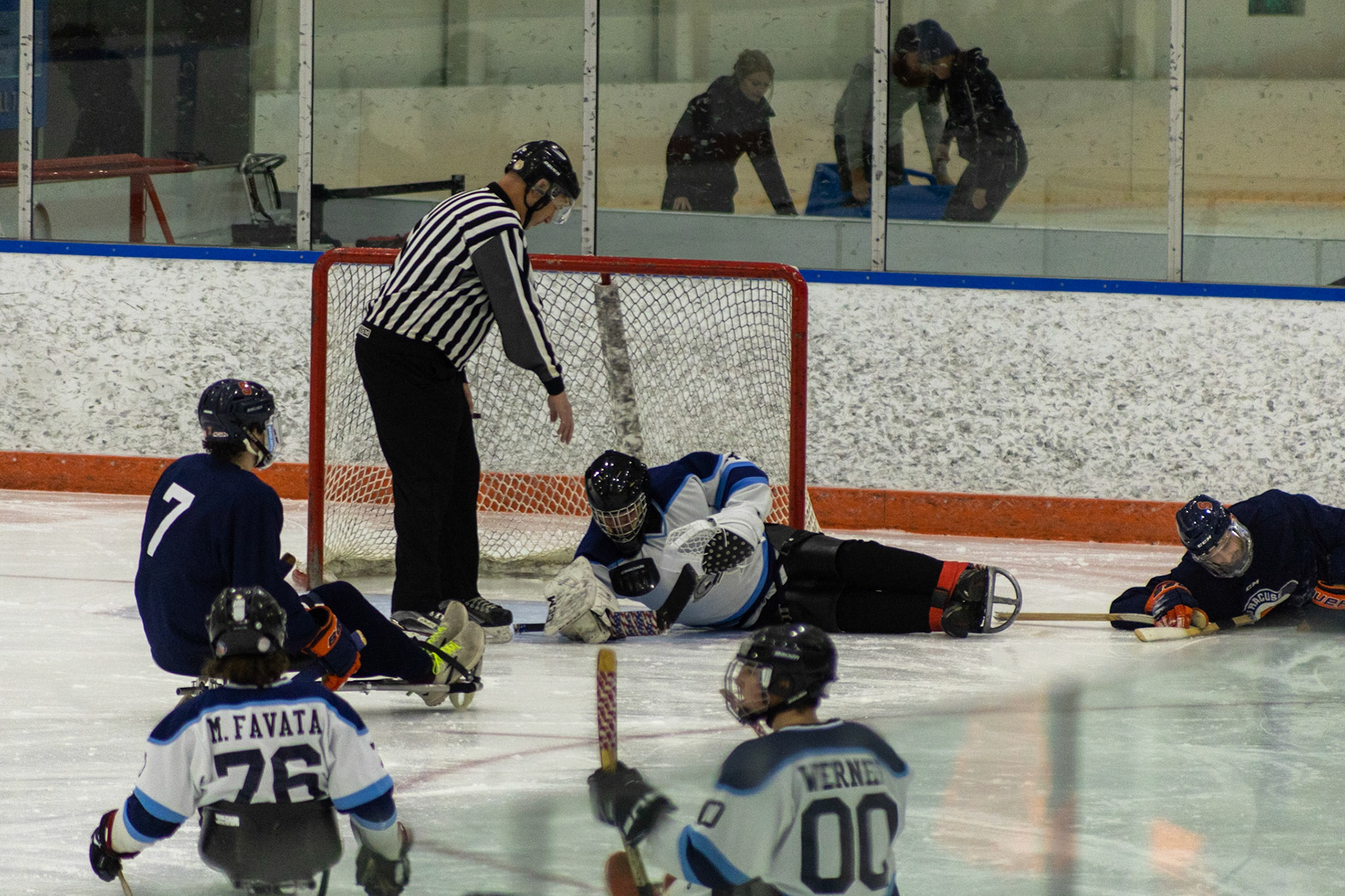 The CNY Flyers, a sled hockey team, played against the Syracuse University Men's Club Hockey team on 11/19/22 at Tennity Ice Skating Pavilion. The game ended with the Flyers scoring 8 to Syracuse 0 with 25 shots on goal by the Flyers compared to Syracuse's 2. While the game was still competitive, it was more for the fun of the sport with smiles shared by all. It was also a new experience for the Syracuse team which consisted of able-bodied individuals who may have never experienced sled hockey. After a successful save by Flyers goalkeeper, Steve Wamp, the referee, Garth Werner, skates over to grab the puck.