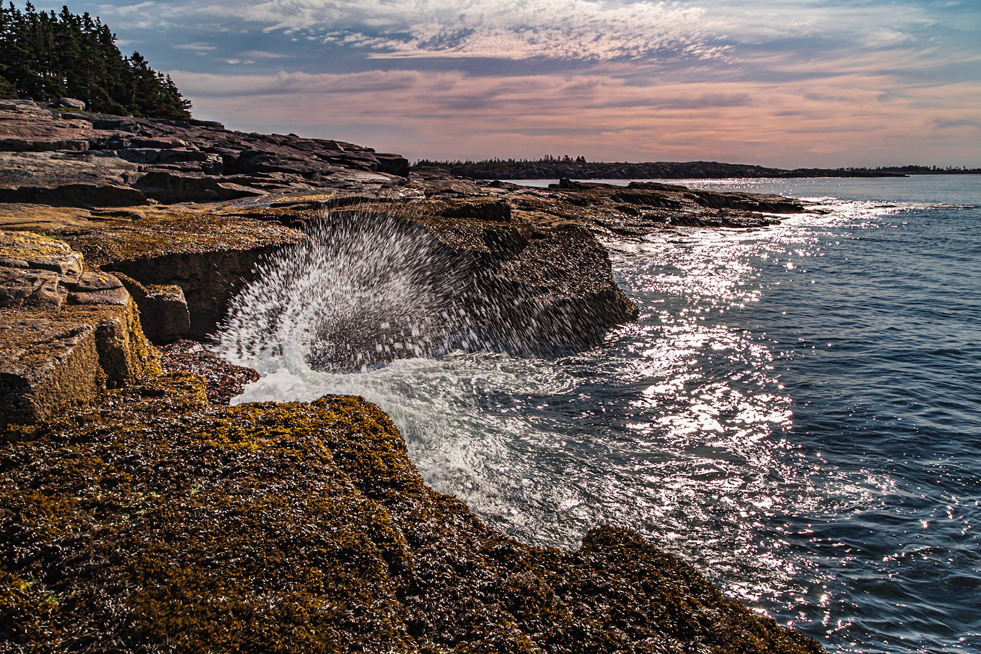 The tide is out but working back in as it splashes against the rocky shore