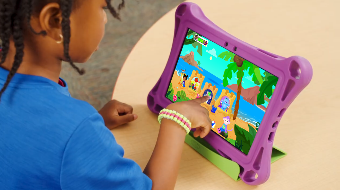A child touches a sandcastle in a vibrant beach scene on a touch tablet with purple safety bumper.