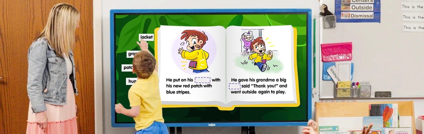 A child drags a word card to a blank space in an eBook on a large touch screen as a teacher watches.