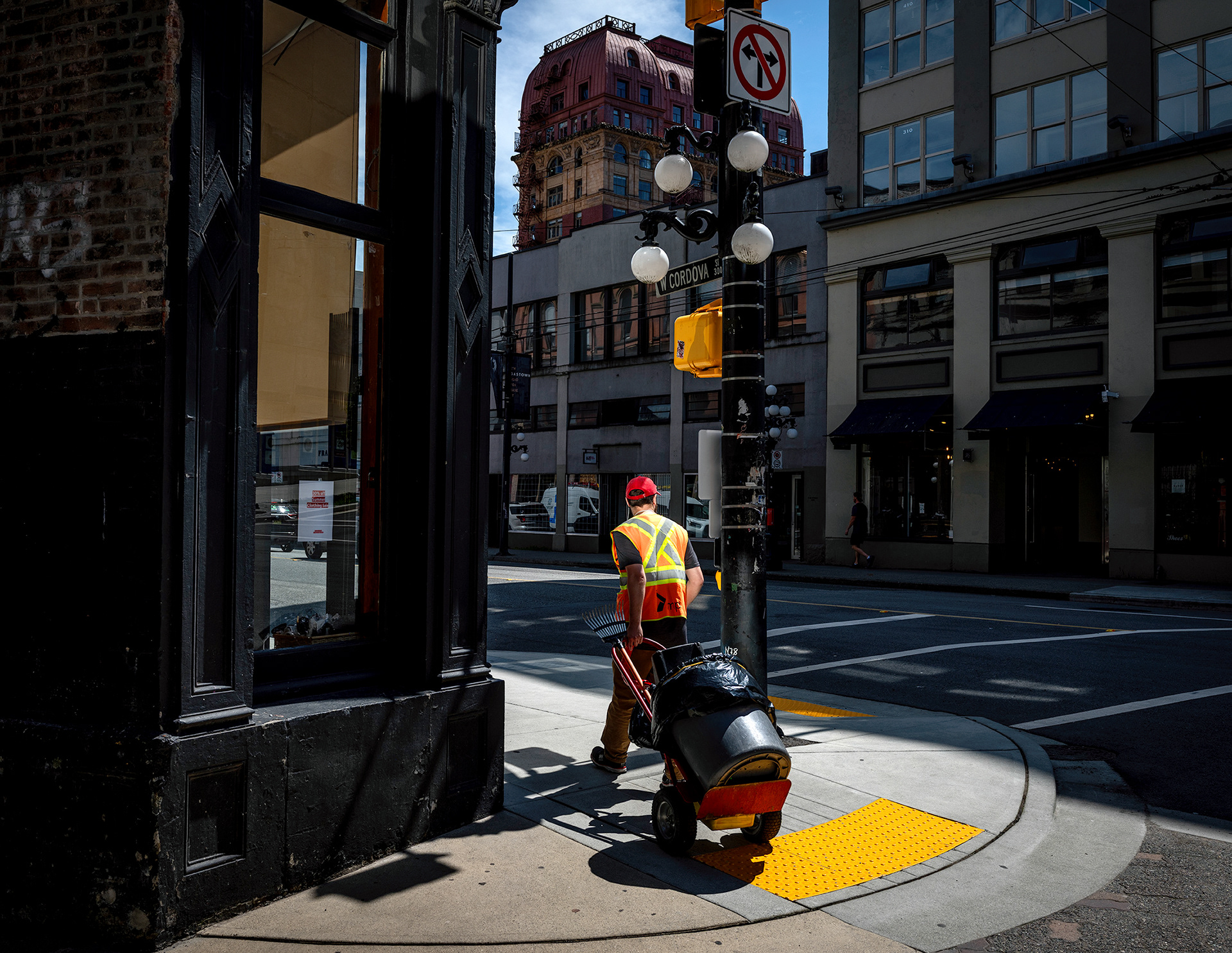 Streetworker with trashcan in tow , reflected light , prominent 'x' work vest, strong color!