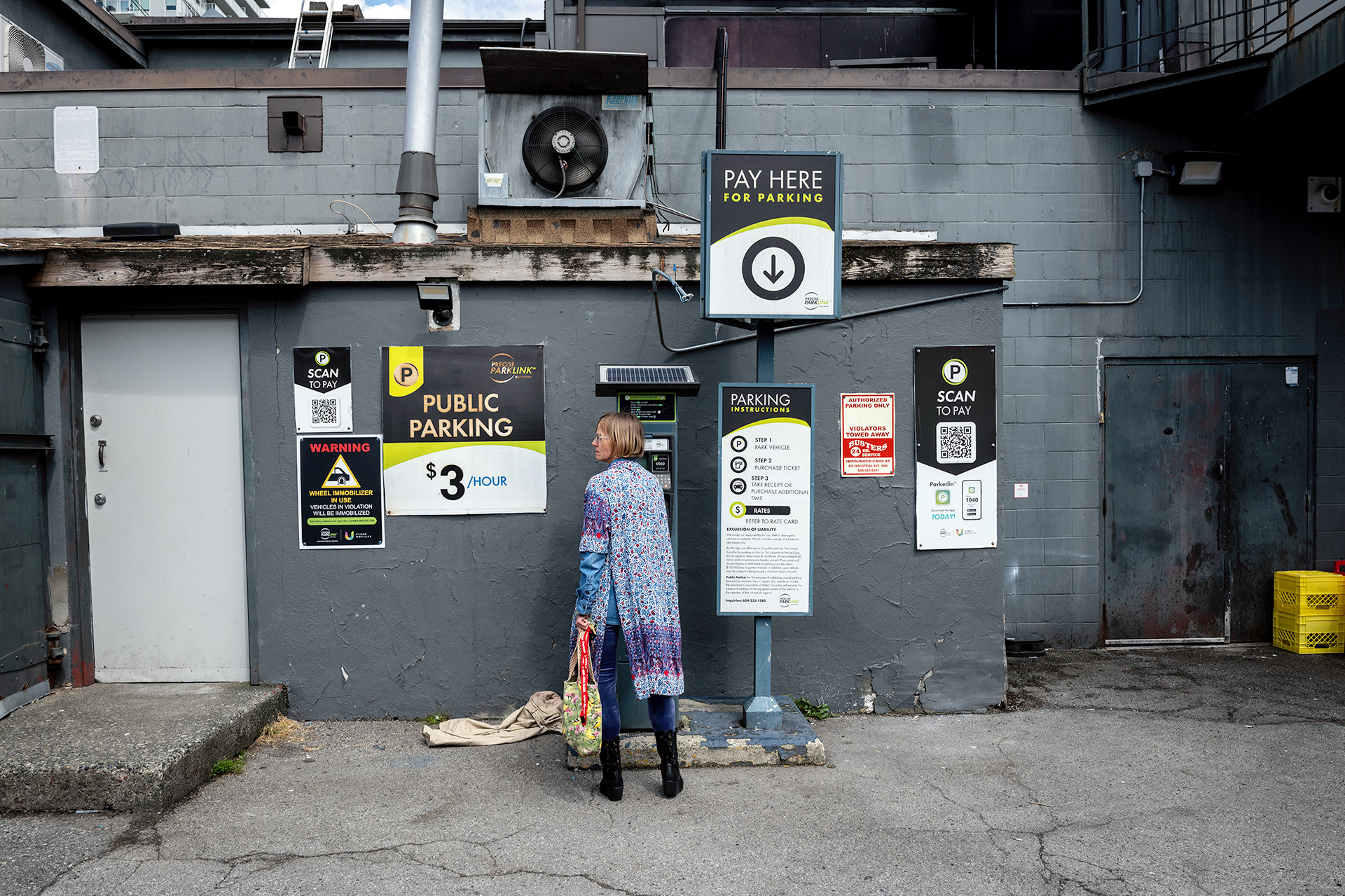 Woman frustrated by pay parking machine and signs, colourful shirt.