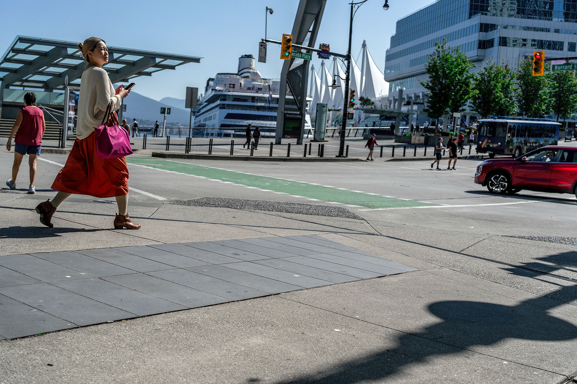 Cruise ship docked in the background, woman striding towards a red car, Canada Place, Vancouver. on sidewalk