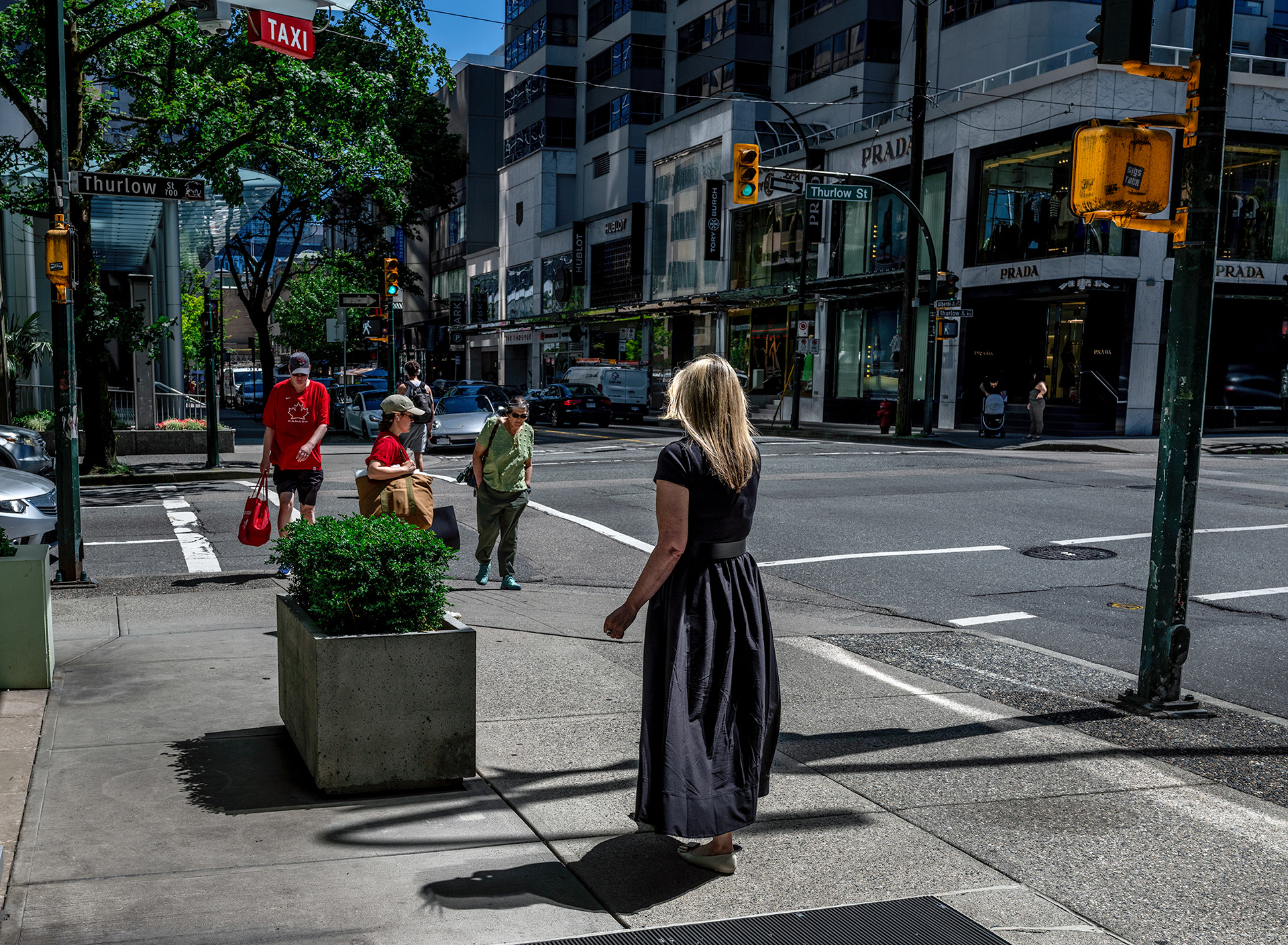 Blonde woman in a black dress, looking like an apparition, approaching passersby.
