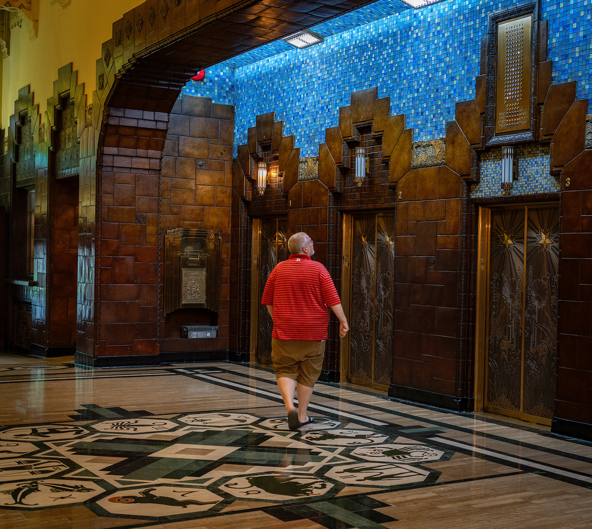 Tile work in Vancouver's Marine Building, man in a red shirt looks pu anticipating his elevator, very colourful scene.
