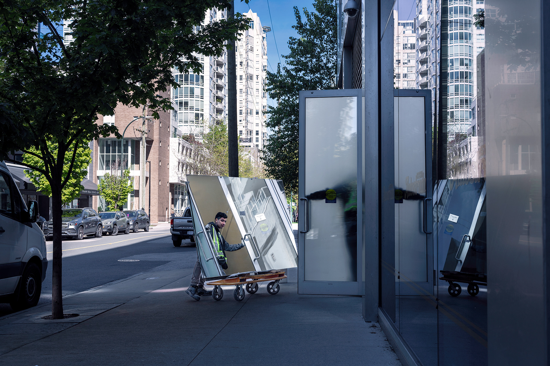 Workman moving a mirror on a sidewalk, mirror reflection creates a whimsical paradox.