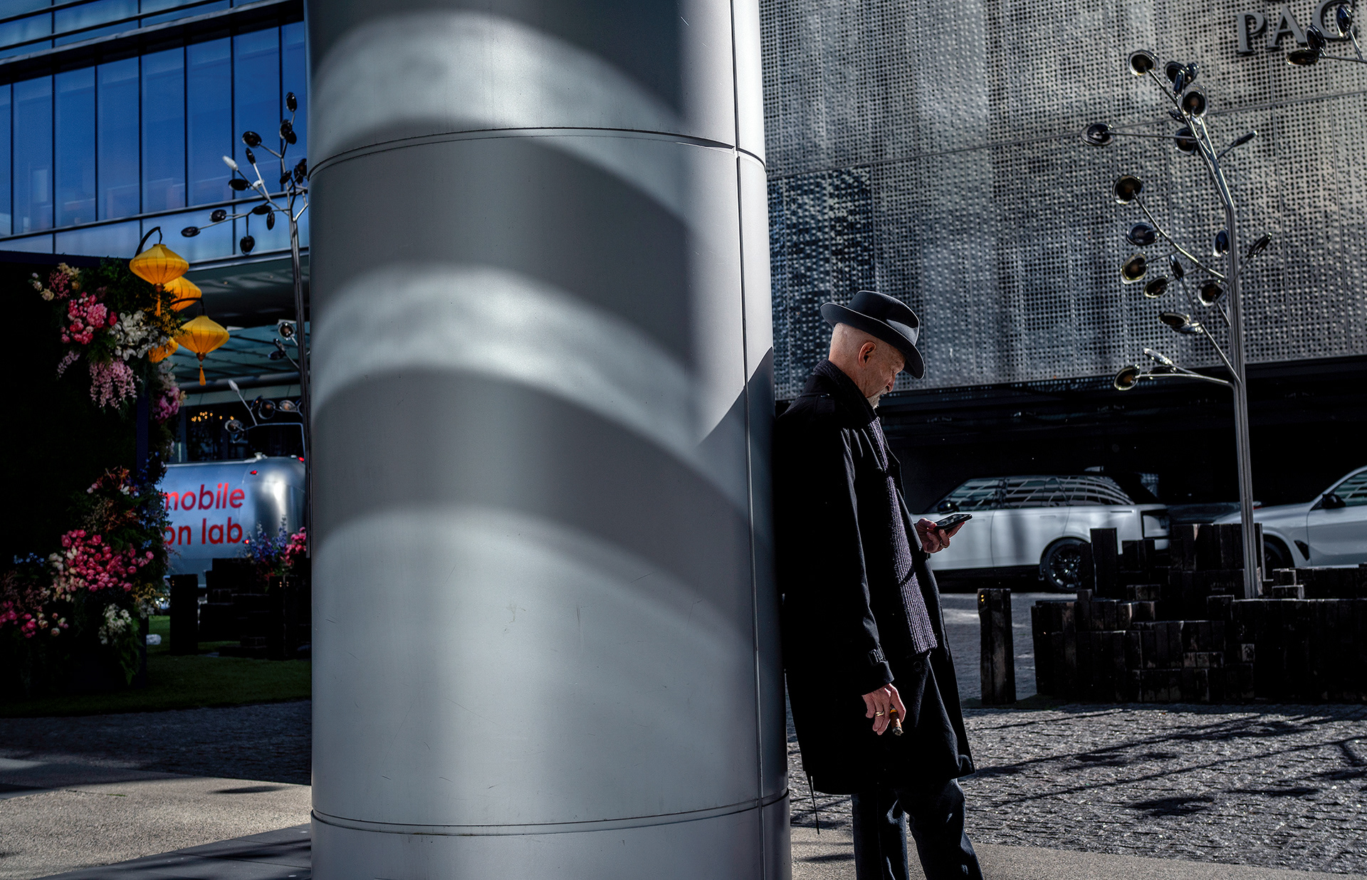 Man leaning against a column, cigar and phone in hand,  yellow lanterns in the background.