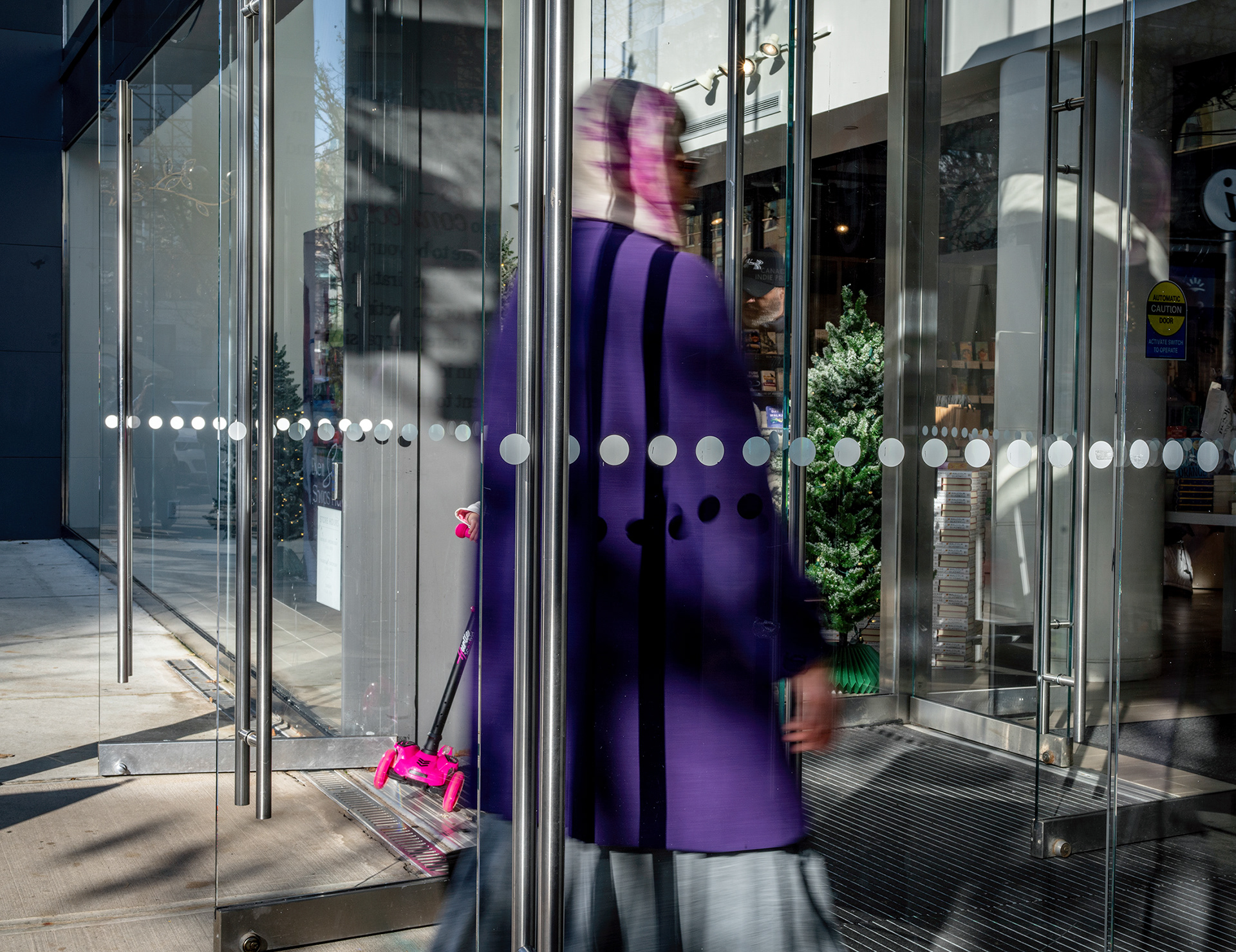 Glass entry door woman in a purple coat with motion blur, magenta child's toy partly visible.