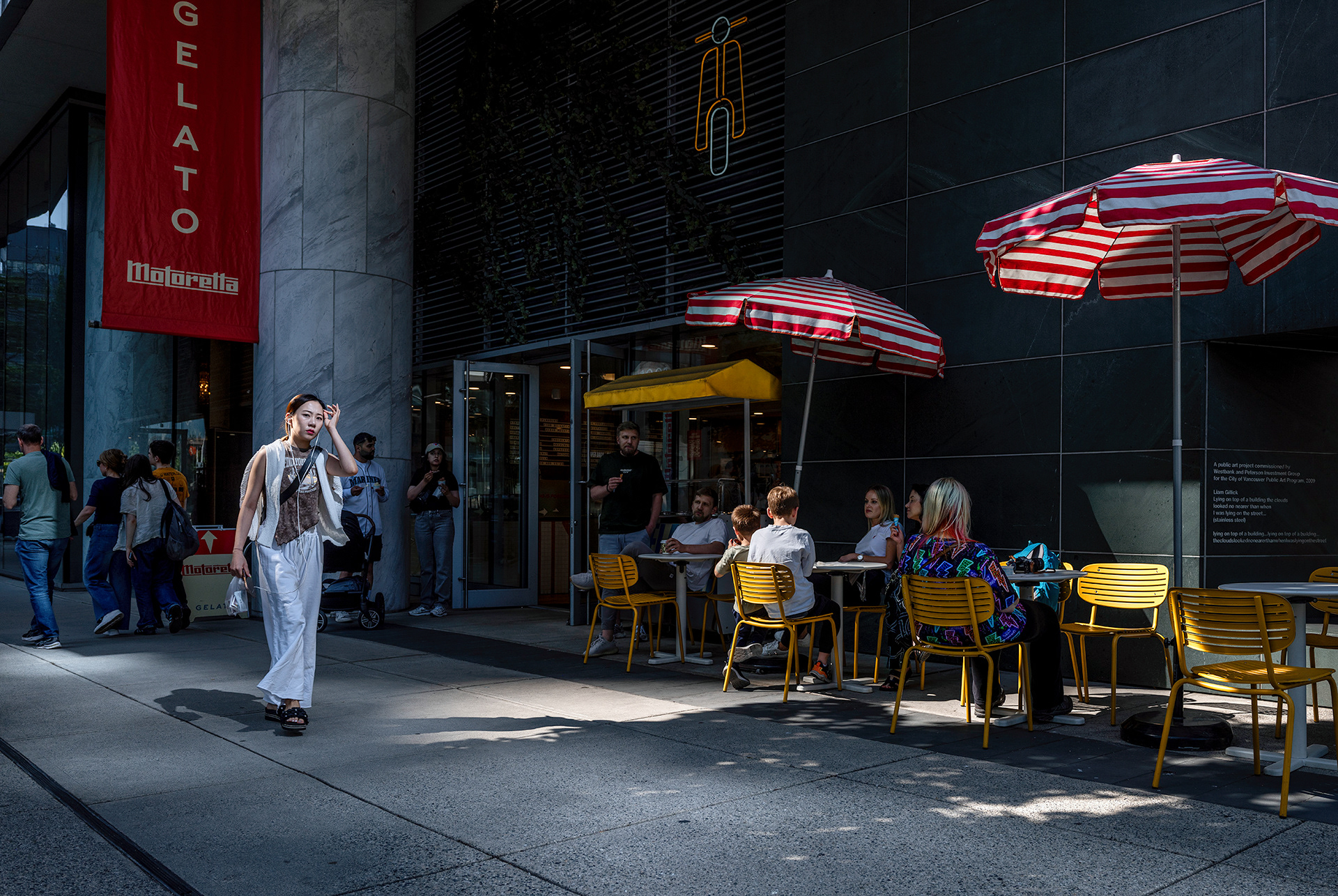 Street photography downtown, Gelato banner red and white striped umbrellas, woman passing by, summer lighting.
