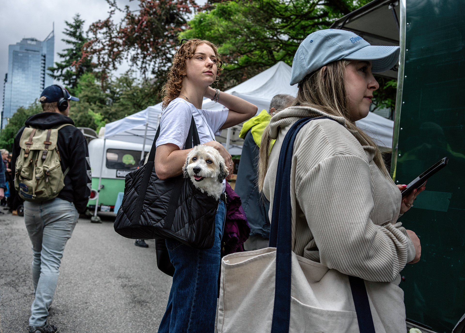Woman with a dog in a bag, the dog is engaging the viewer, the woman is oblivious.