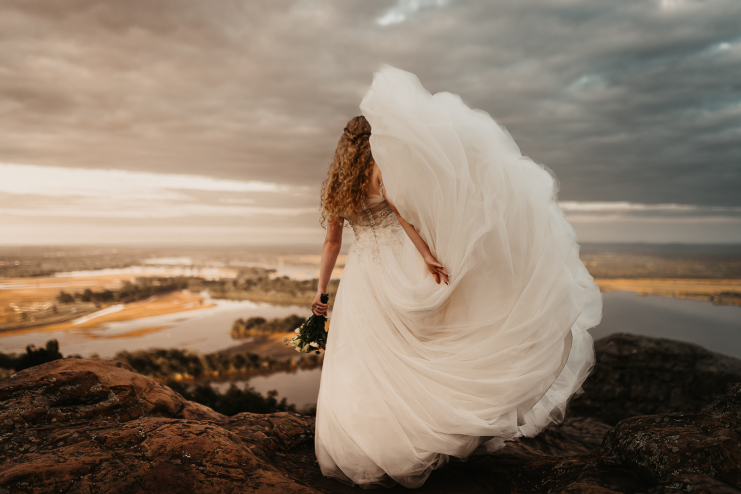 epic photo of bride standing on the edge of petit jean mountain at sunset
