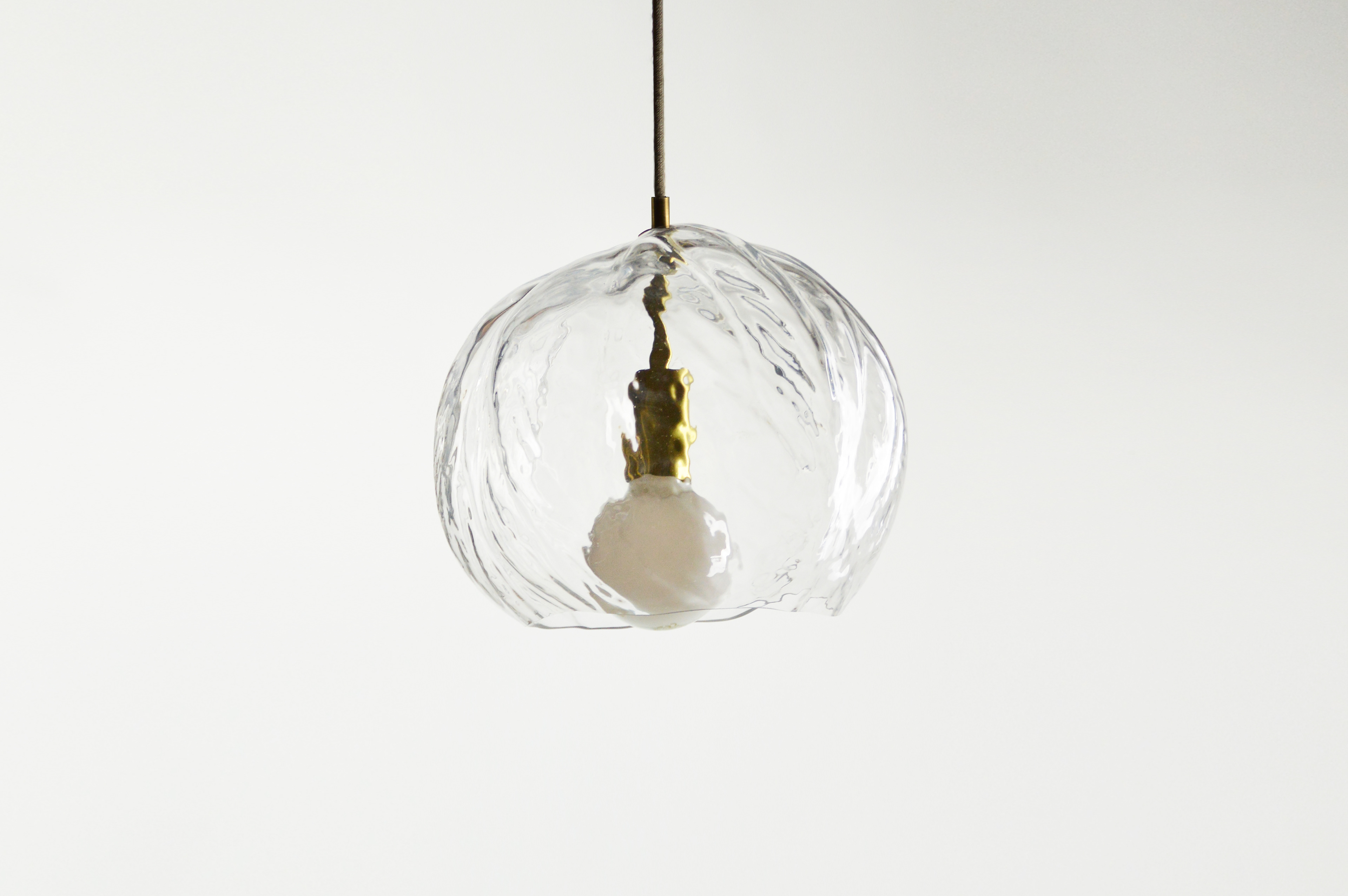 Suspension lumineuse en verre soufflé. Forme organique obtenue par soufflage dans des feuilles. Impression de la texture et des nervures de l’espèce végétale à la surface de l’objet.