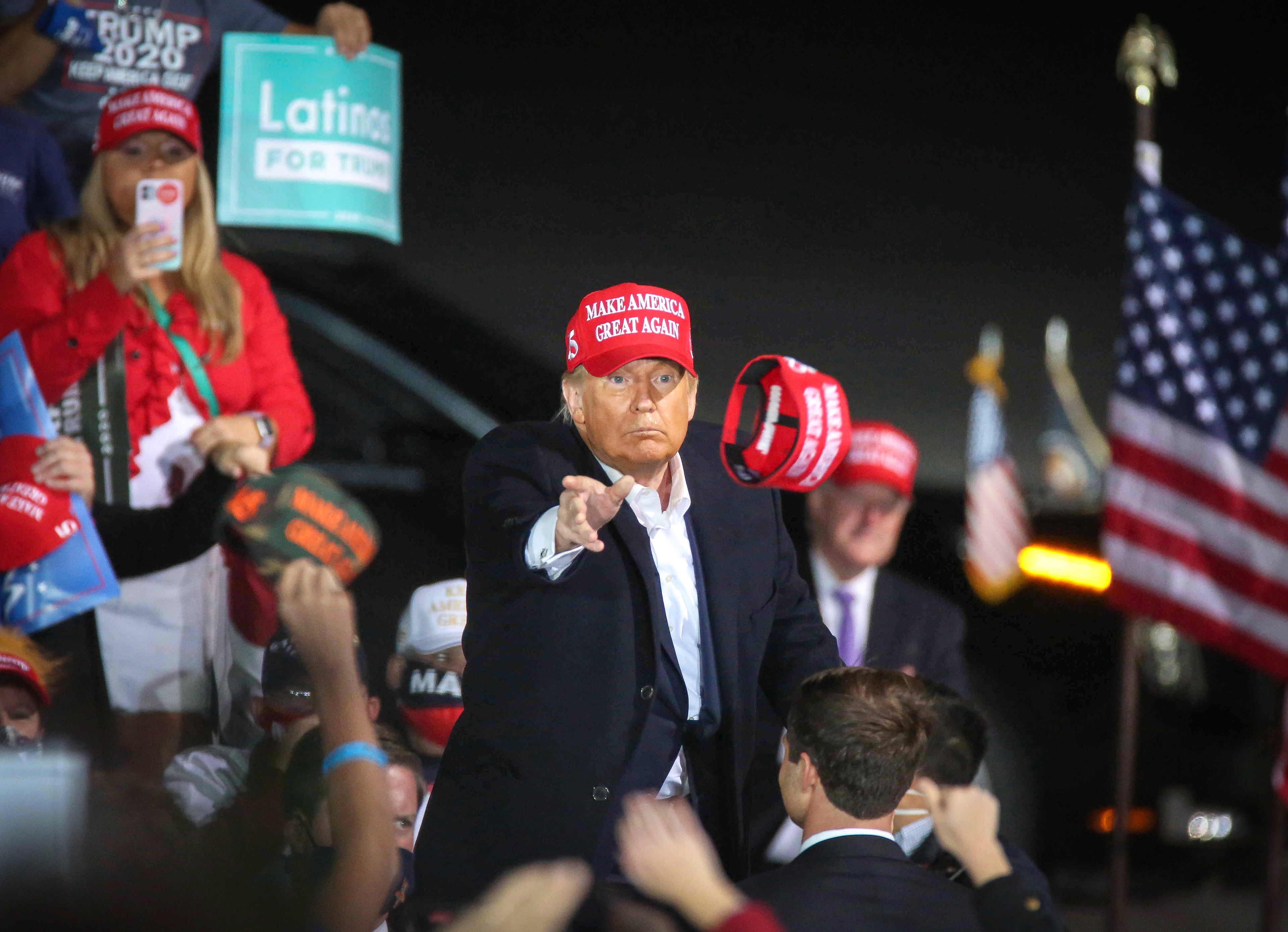 U.S. President Donald Trump tosses a Make America Great Again hat into a crowd of thousands after speaking at the Des Moines International Airport during a rally in Iowa on Wednesday, Oct. 14, 2020.