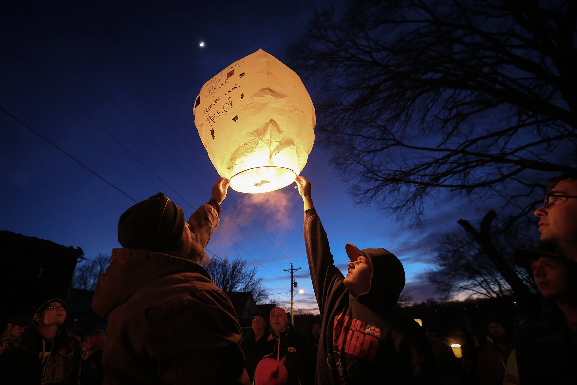 Jason Reyes of Fort Dodge, Iowa, left, tries to release a paper lantern during a candlelight vigil for the deaths of Amy Devlin, 25, her 6-month-old son, Bryce Devlin, and 5-year-old Joseph Kennedy, who were all killed in a house fire in Fort Dodge on Sunday, Feb. 22, 2015.