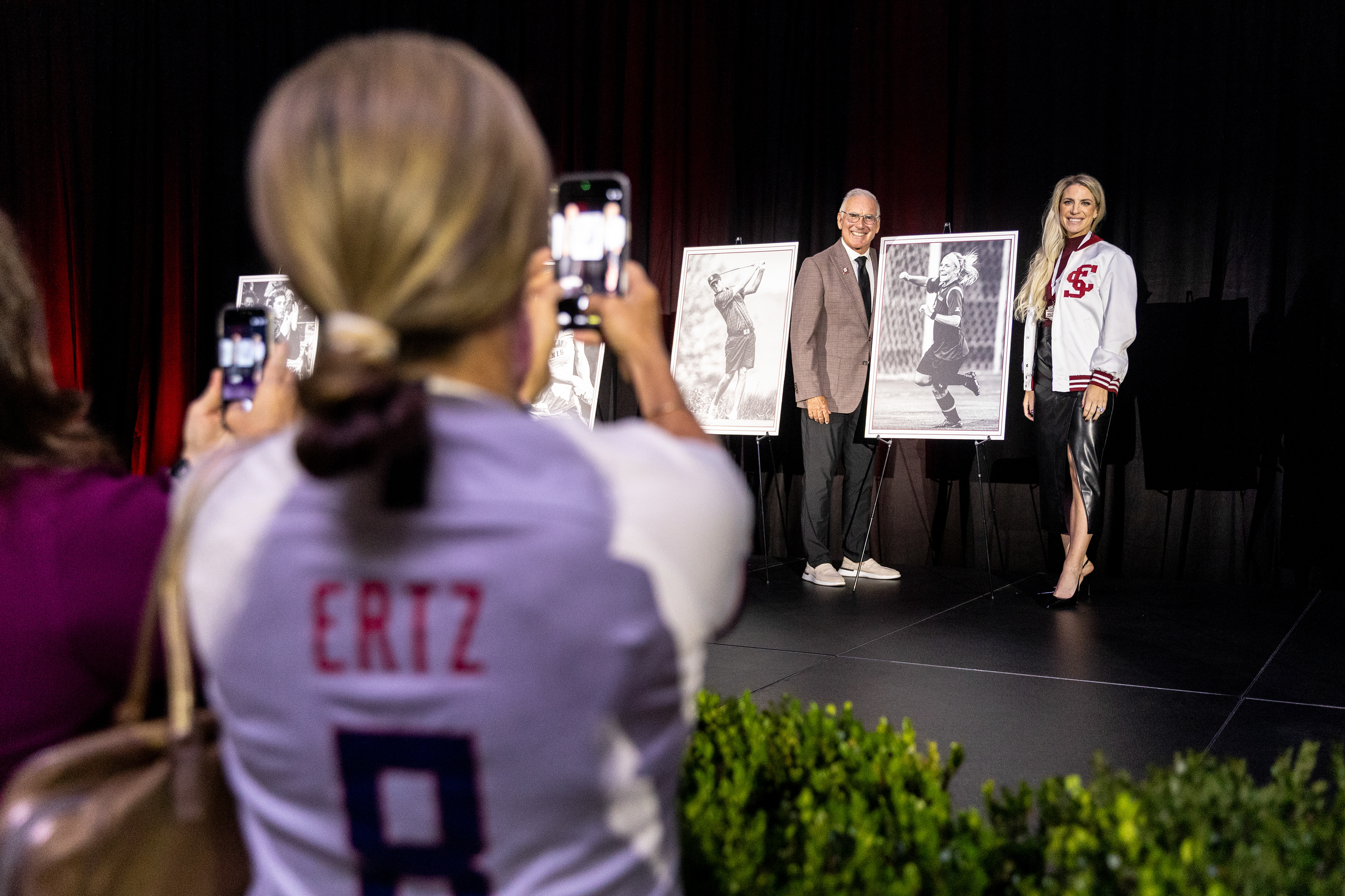 Santa Clara women’s soccer alumna Brandi Chastain, wearing a Julie Ertz jersey, takes a photo of her husband and Santa Clara women’s soccer Coach Jerry Smith and Julie Ertz ’13 after Ertz was inducted into the Santa Clara Athletics Hall of Fame on May 2, 2026 at the Leavey Center. (Nina Glick/The Santa Clara)
