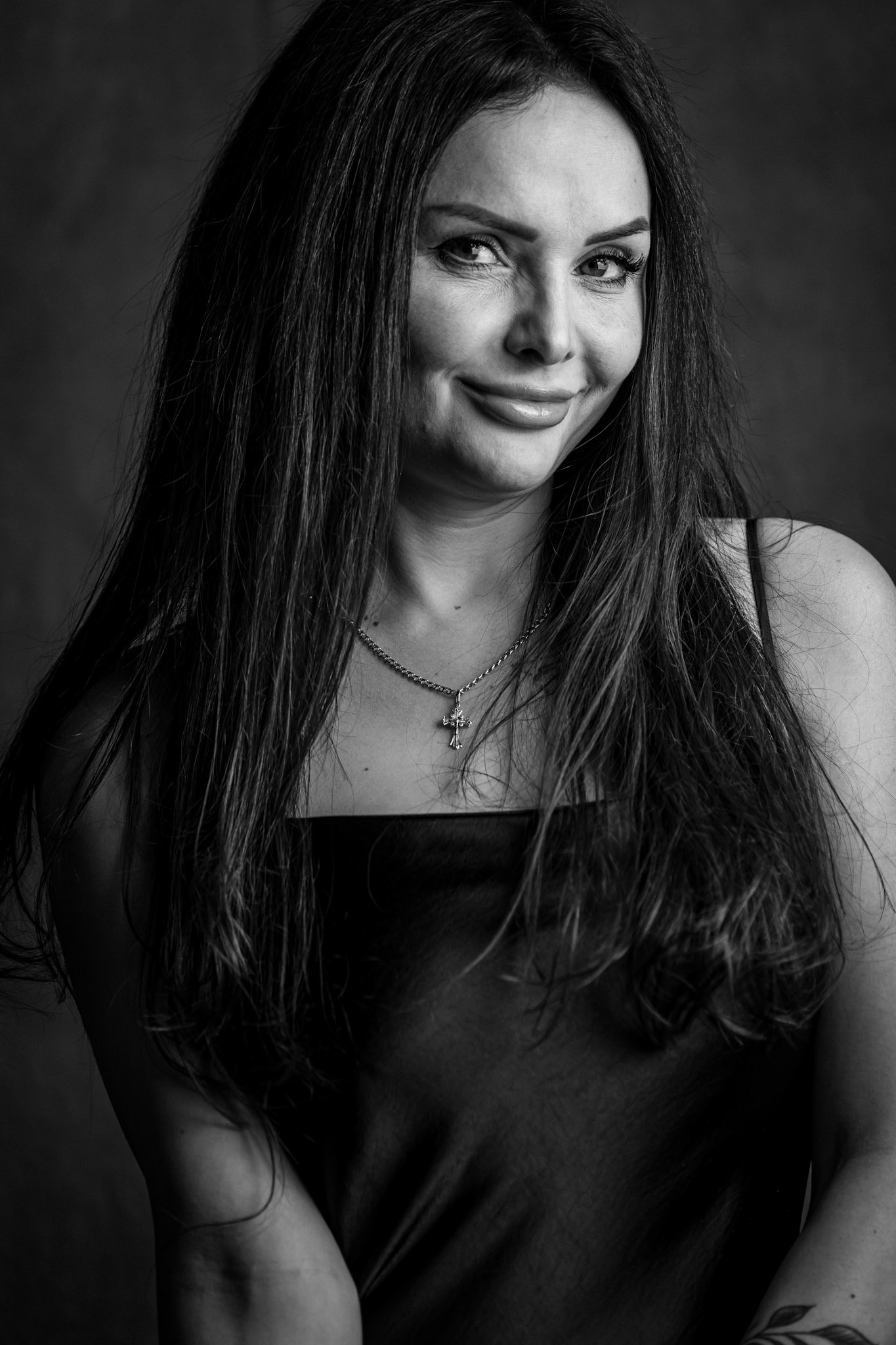 Cinematic black-and-white studio portrait of a woman with long dark hair and a direct, confident expression.