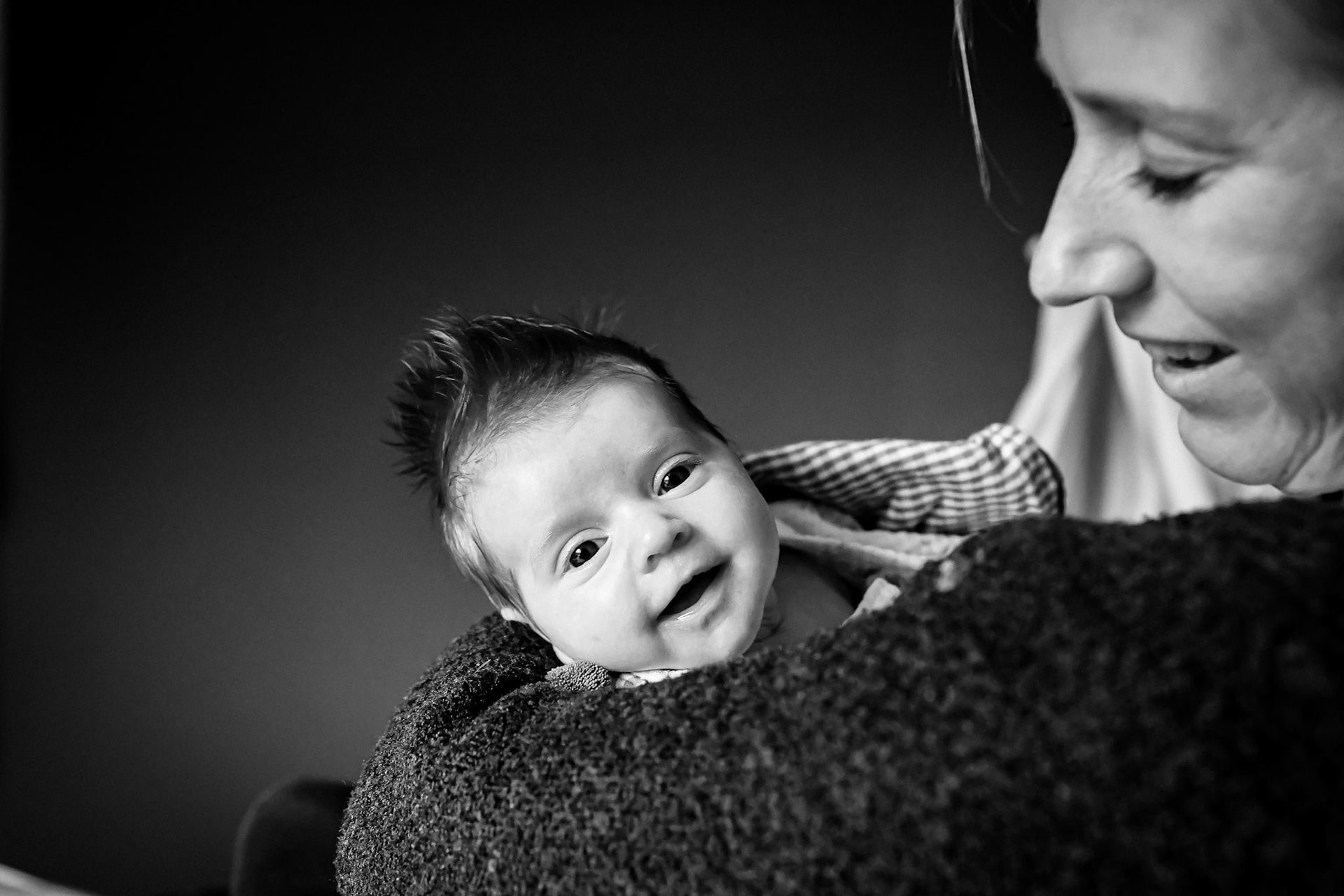 Tender black-and-white portrait of a smiling baby with a parent.
