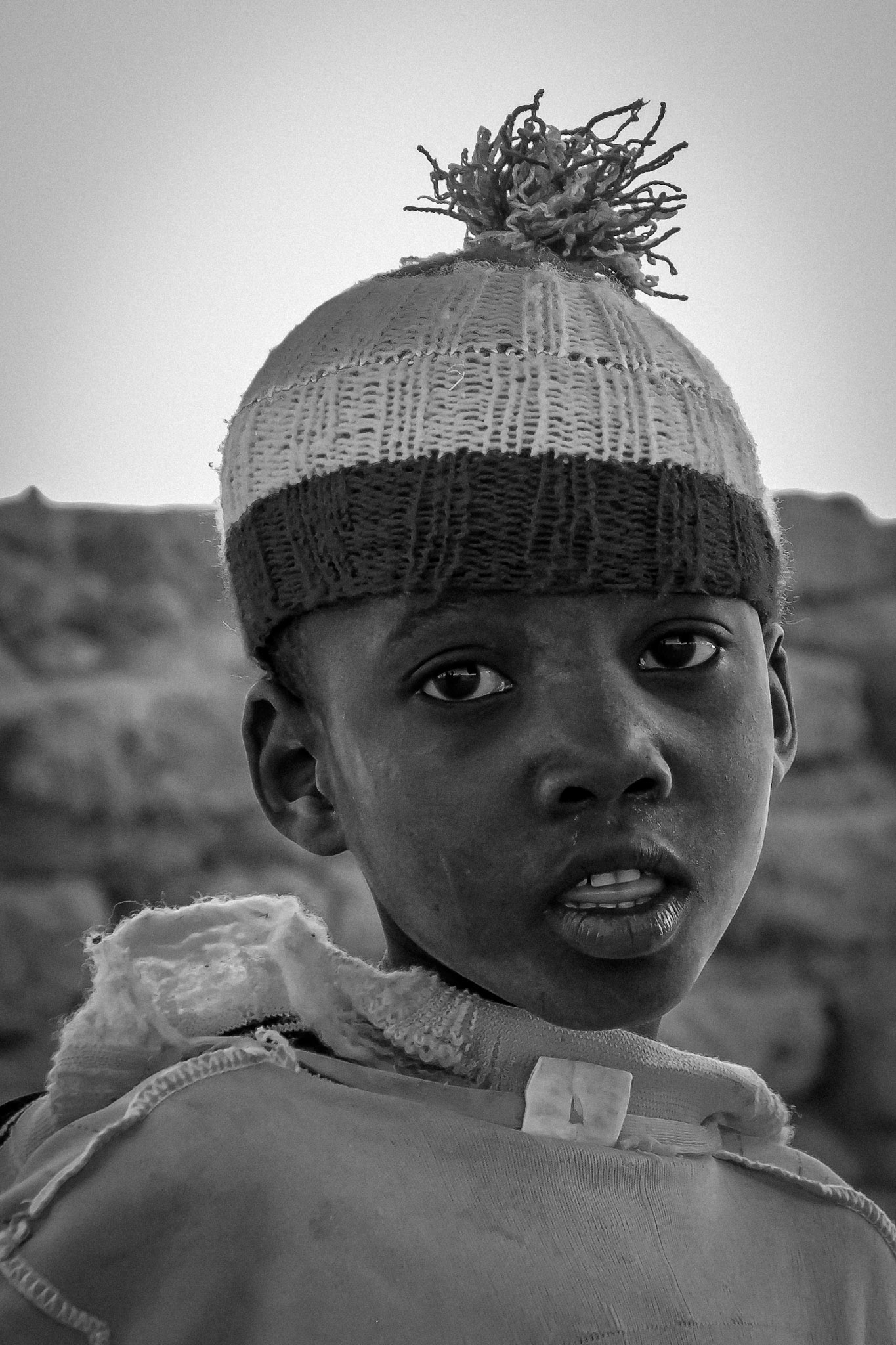 Black-and-white environmental portrait of a child wearing a woven hat.