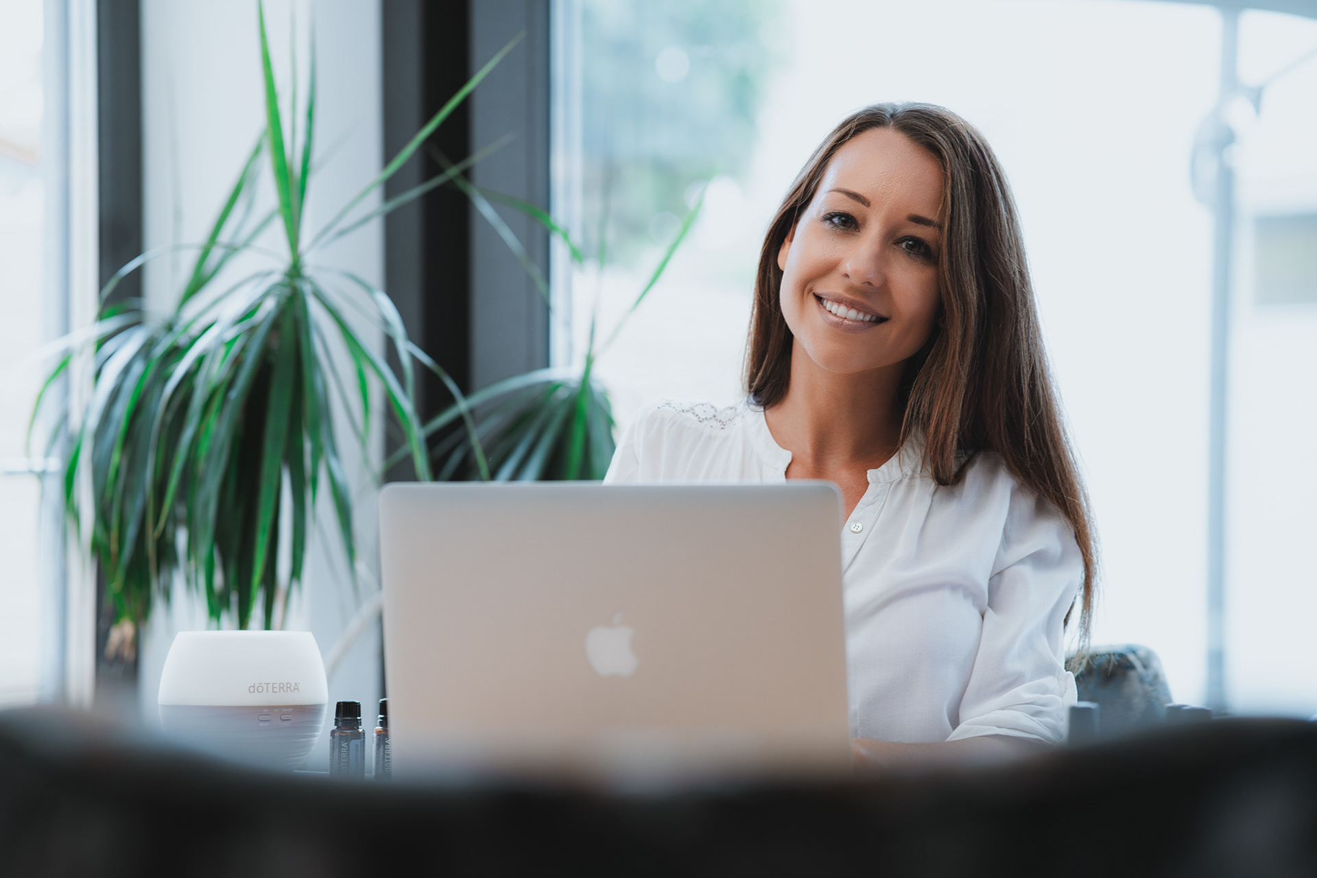 Authentisches Business-Lifestyle-Fotoshooting in Regensburg: Lächelnde Frau arbeitet am Laptop in einem hellen Büro mit Zimmerpflanzen, moderne Imagefotografie von Medusa Fotografie Regensburg