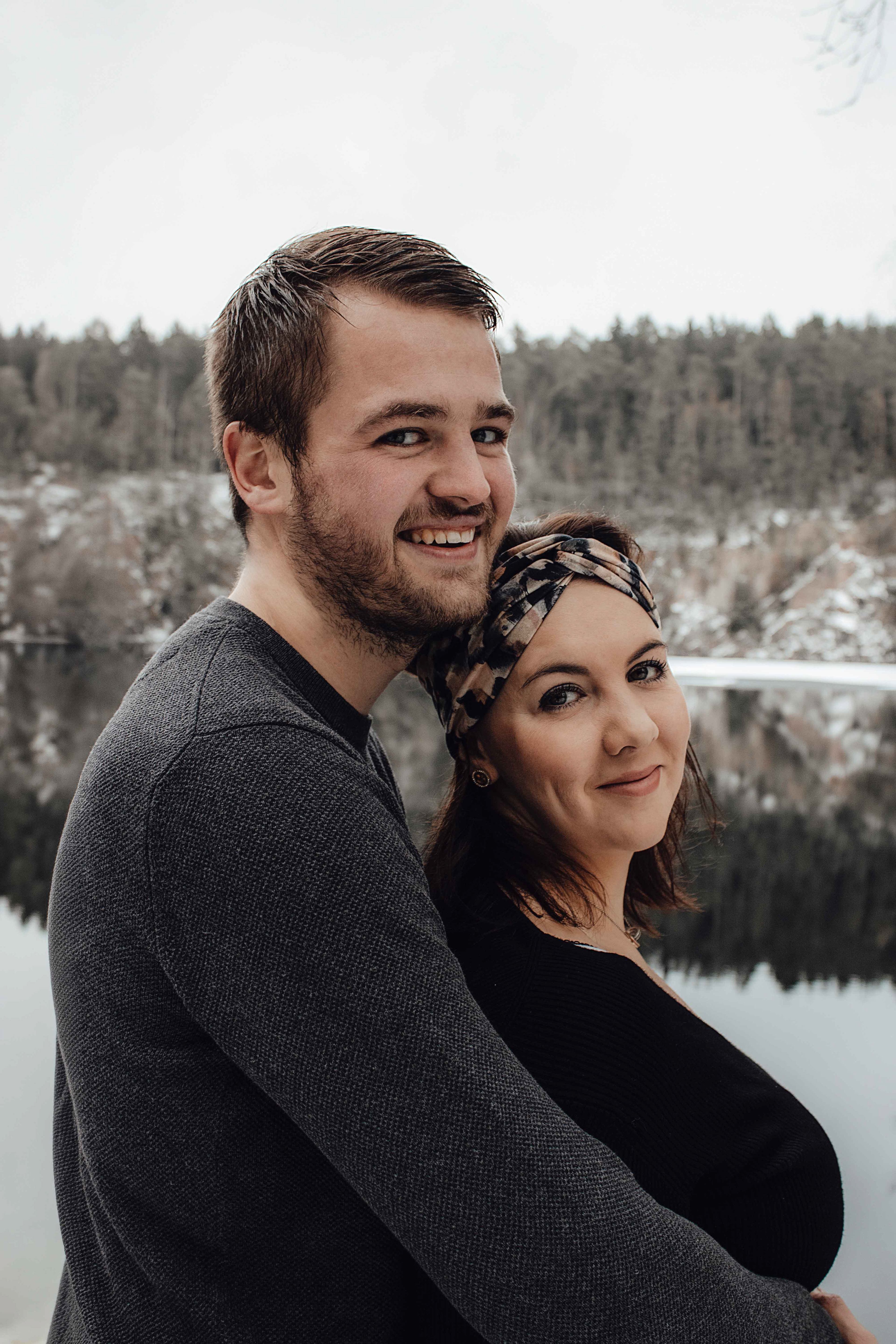 Ein verliebtes Paar steht eng umschlungen auf einem Holzsteg an einem idyllischen See, fotografiert von Medusa Fotografie