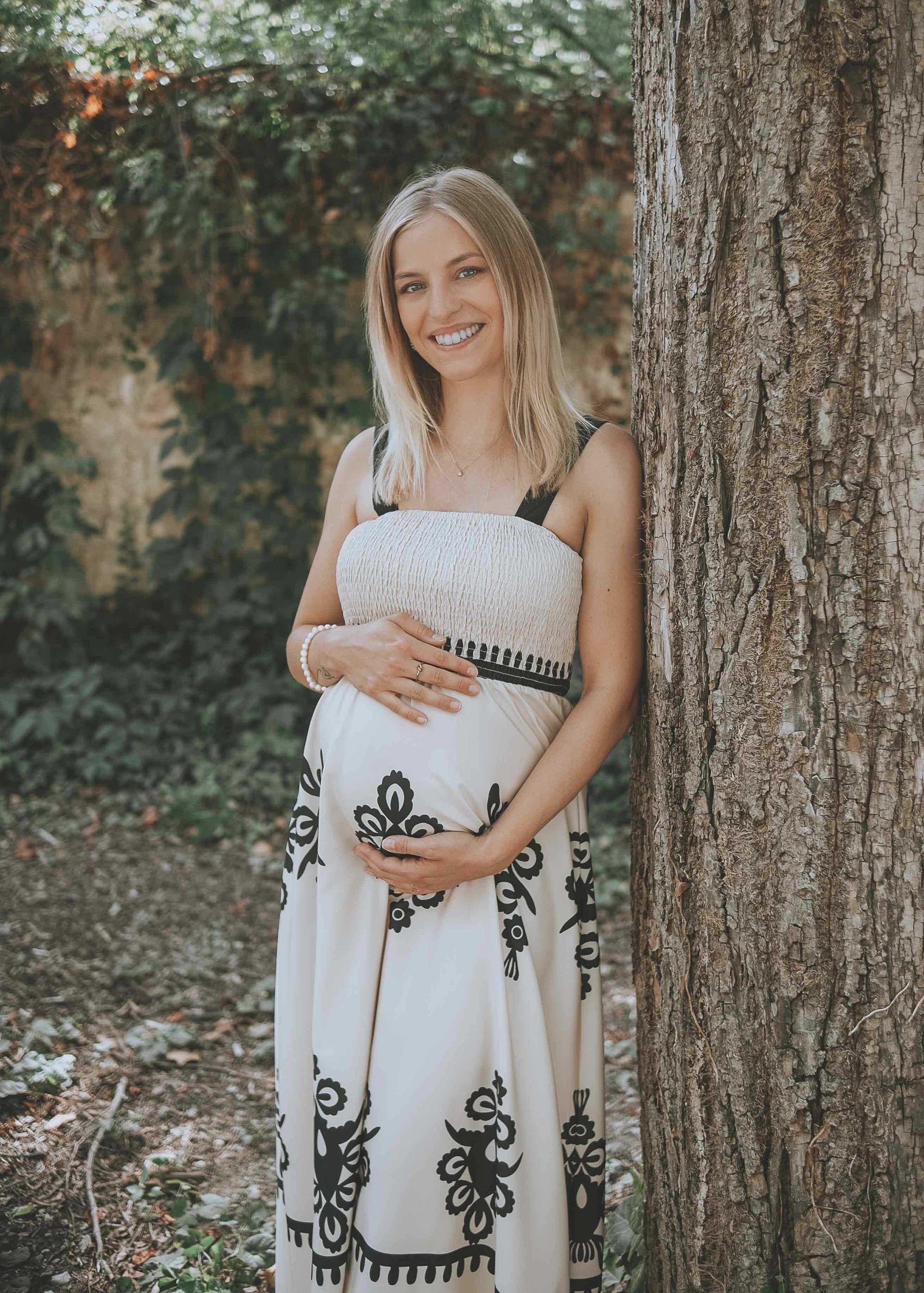 Natürliches Babybauch-Shooting im Freien, lächelnde Schwangere lehnt an einem Baum, Medusa Fotografie – dein Fotograf in Regensburg