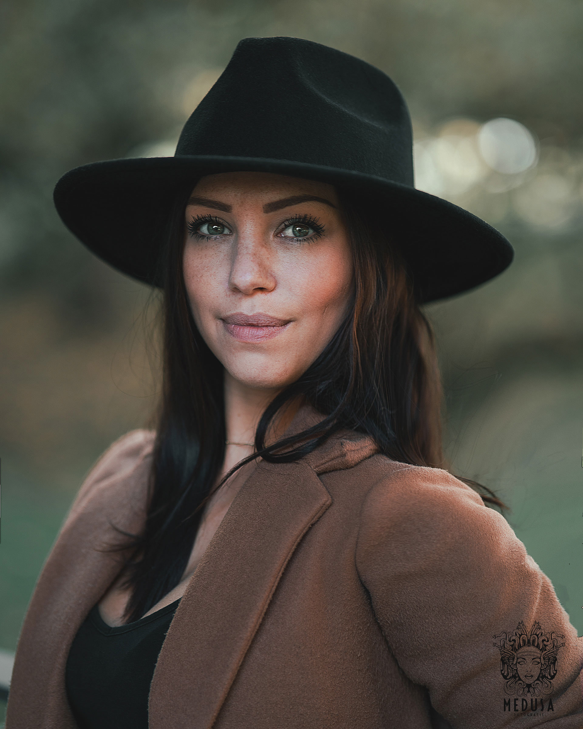 Elegantes Porträt einer Frau mit Hut und braunem Mantel, fotografiert im Stadtpark Regensburg von Medusa Fotografie