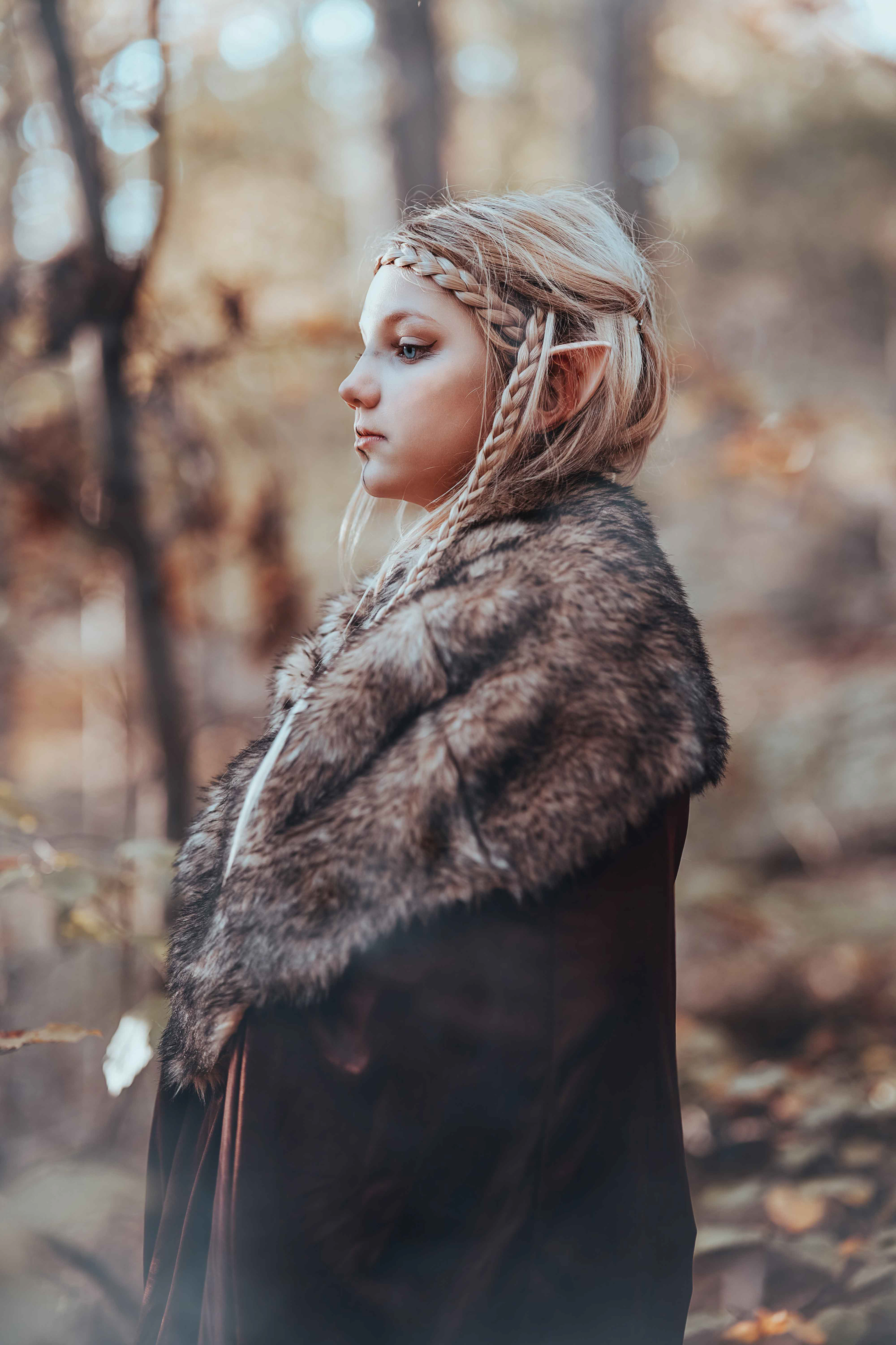 Atmosphärische Outdoor Fotografie einer Elfen Kriegerin, die im herbstlichen Wald steht und einen Pfeil auf ihrem Bogen eingelegt hat. Professionelles Fantasy Fotoshooting von Medusa Fotografie mit Fokus auf die wehrhafte Pose und die Naturkulisse.