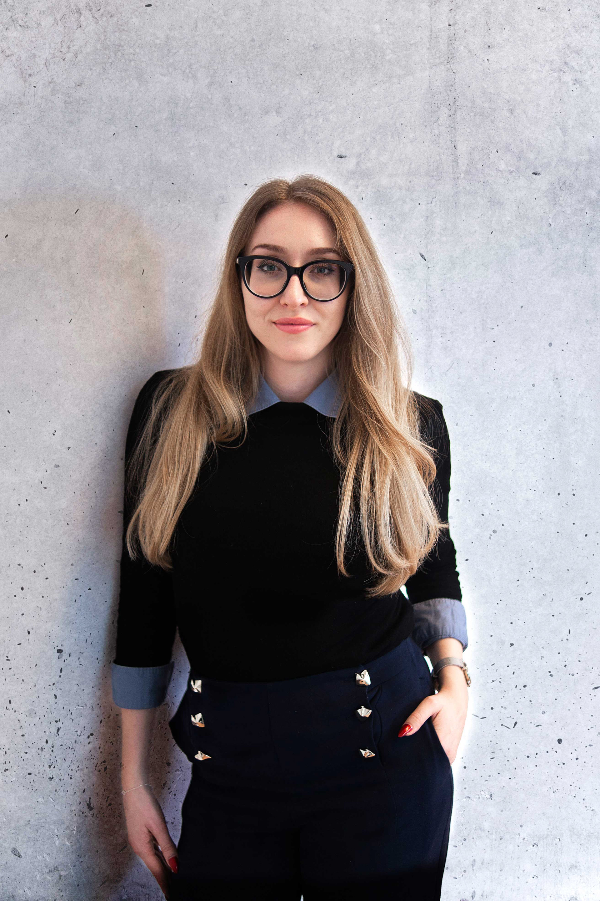 Professionelles Imagefoto für Business-Branding in Regensburg: Junge Frau in modernem Business-Outfit vor grauer Sichtbetonwand, fotografiert von Medusa Fotografie Regensburg