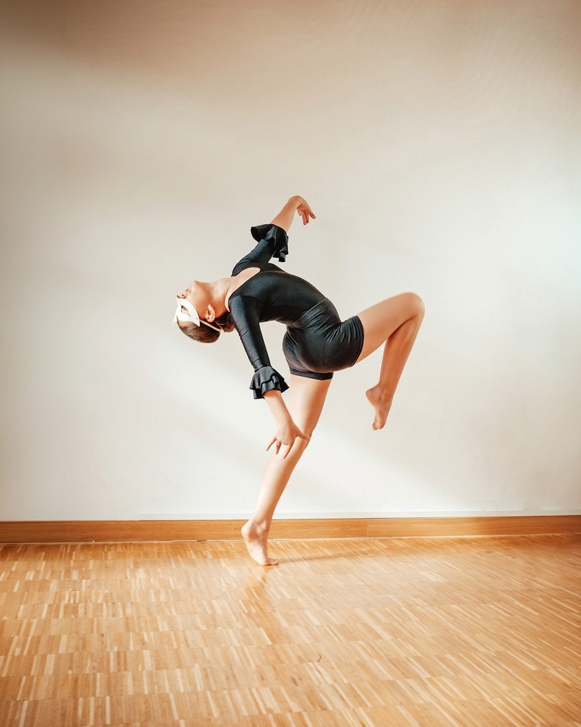 Eine Tänzerin vollführt eine anspruchsvolle, rückwärts gebeugte Pose auf dem Parkettboden der Tanzschule.