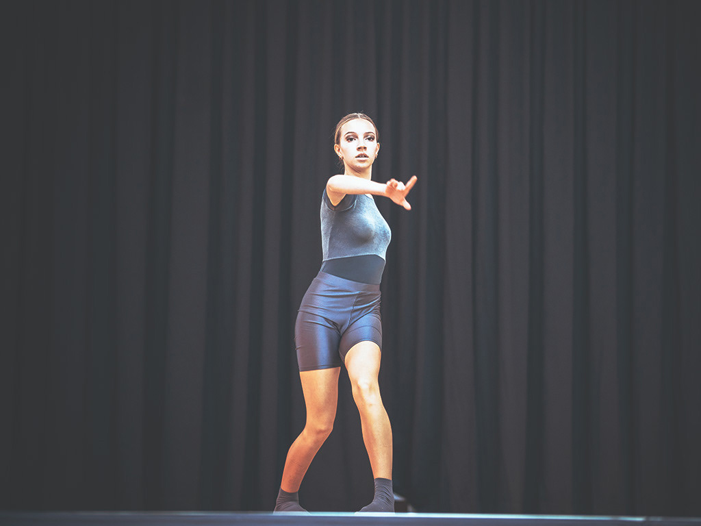 Eine Tänzerin der Tanzschule Sophia Eis in einem blauen Samt-Body zeigt eine fokussierte Pose auf der Bühne vor einem schwarzen Vorhang