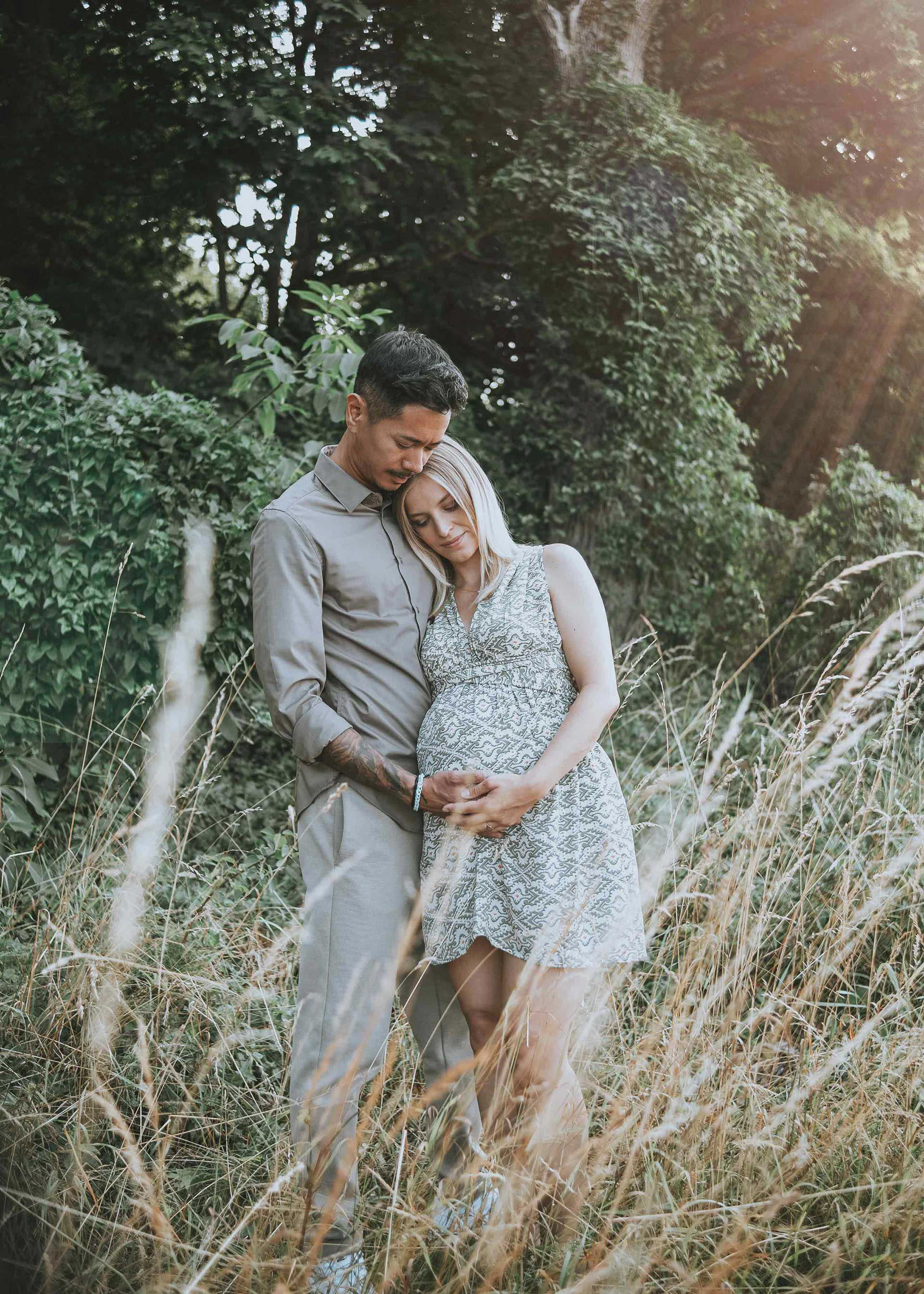 Gefühlvolle Aufnahme eines Paares in einer hohen Gräserwiese beim Babybauchshooting in Regensburg im Abendlicht