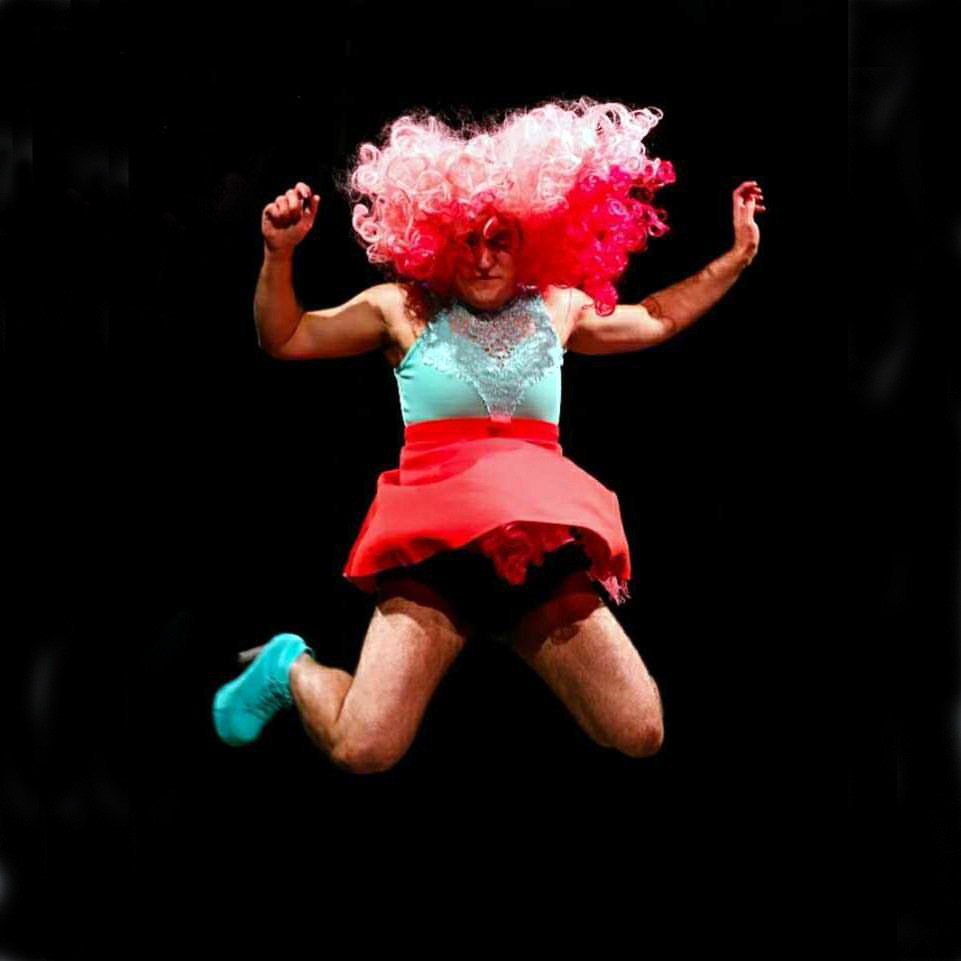 I am mid jump and my skirt is flying up and so is my hair, parts of my face are exposed and no longer covered by my hair. Both my knees are bent and only my left shoe is shown. Both my hands are in the air above my head.
