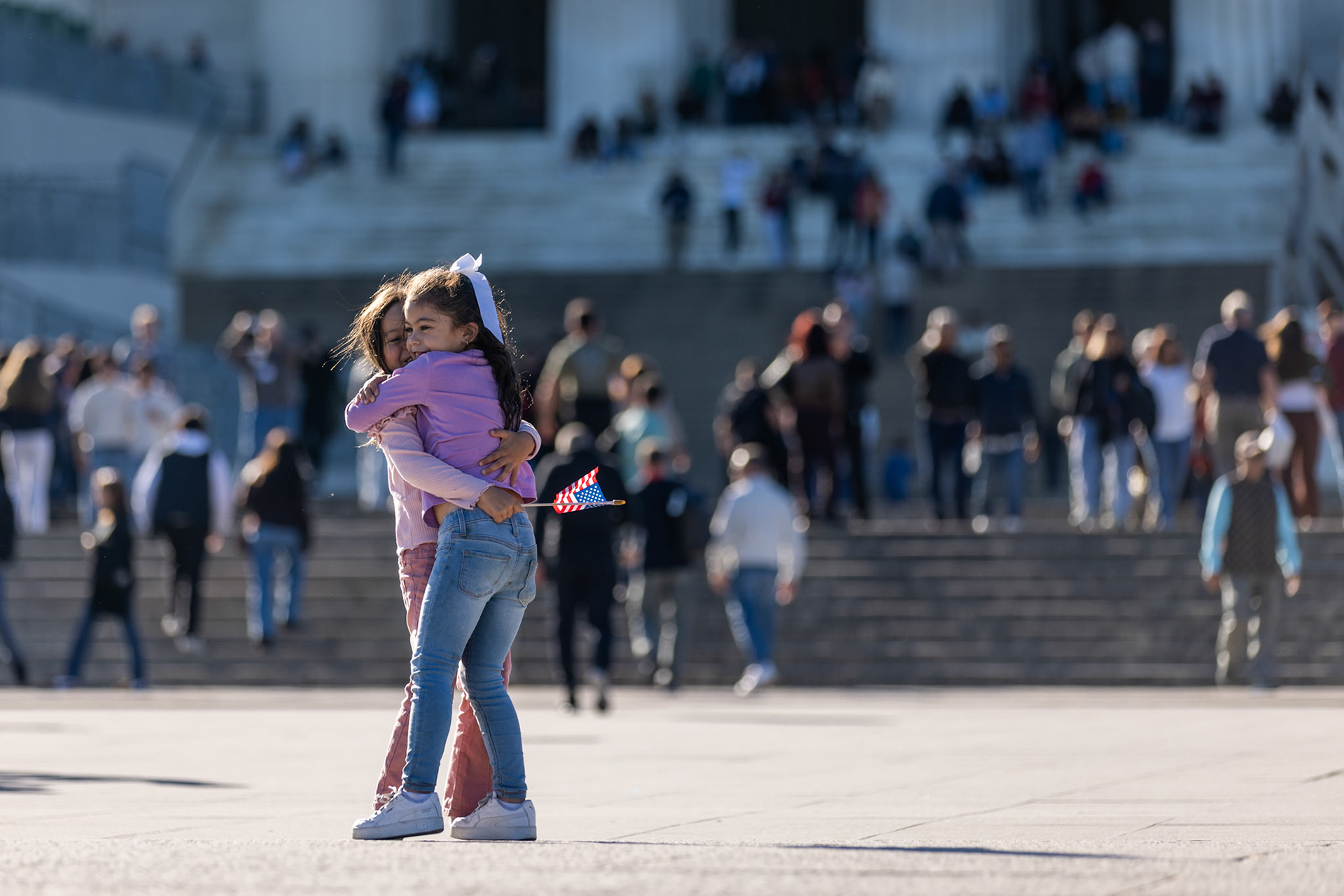Holding American flags, two girls embrace in front of the Lincoln Memorial during a Unite the DMV rally on Oct. 17, 2025. The protest, which featured speakers and dancing, brought together government employees, citizens, and veterans in an effort to defend democracy on the eve of the No Kings protests.