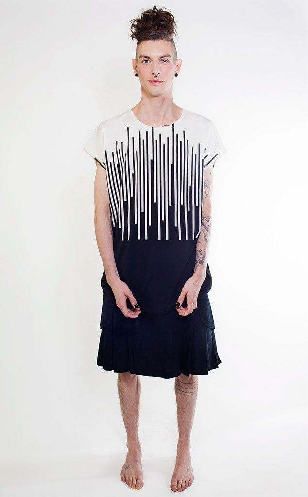 colour photograph of a man in a black kilt and a black and white vertically striped top.. The sided of his head are shaven, The long hair on the top of his head is worn in a beehive style. He has half open fists. His lips and cheeks have an orange hue.