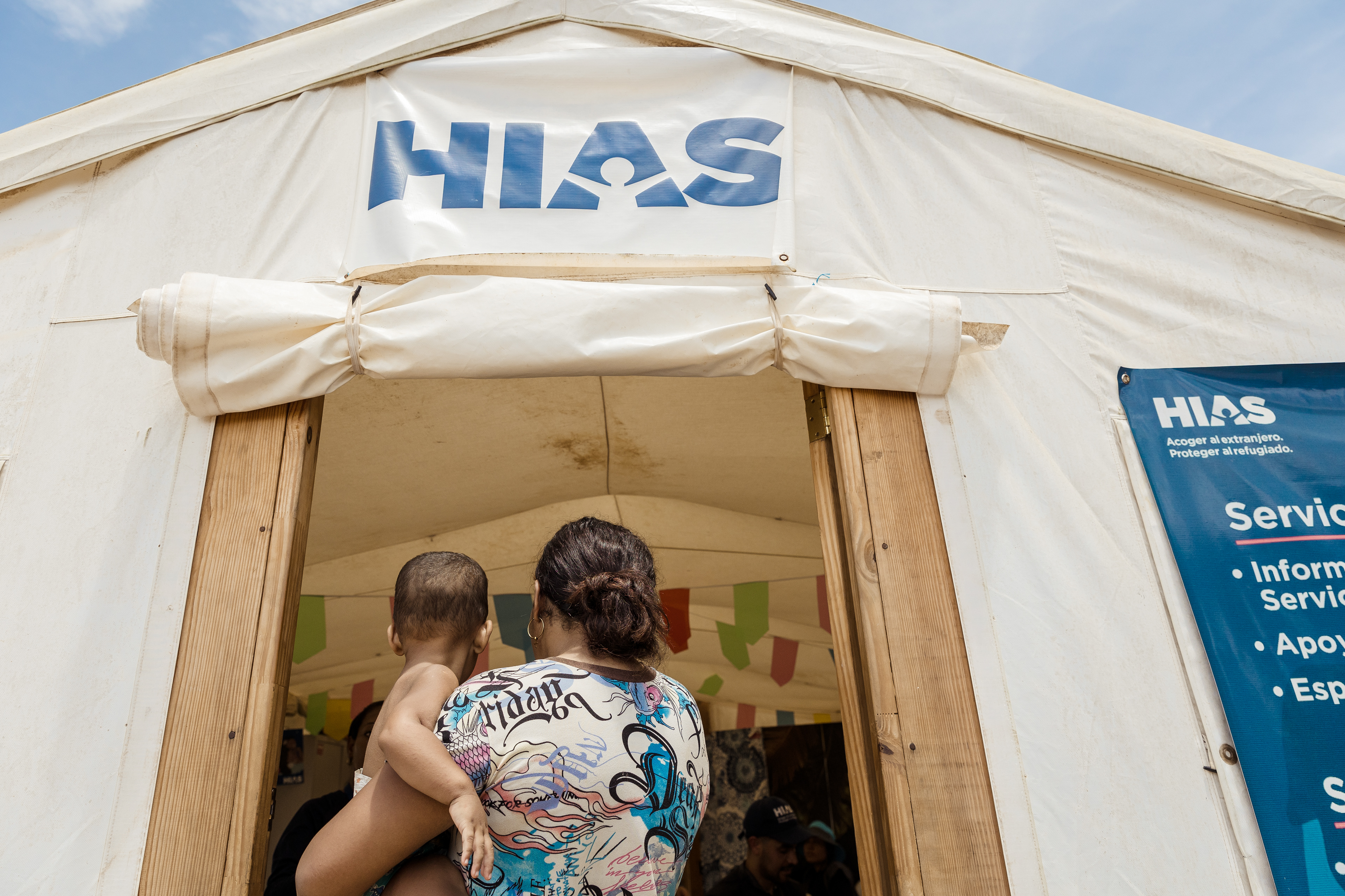A migrant mother and child stand at the entrance of the HIAS support tent in Lajas Blancas.