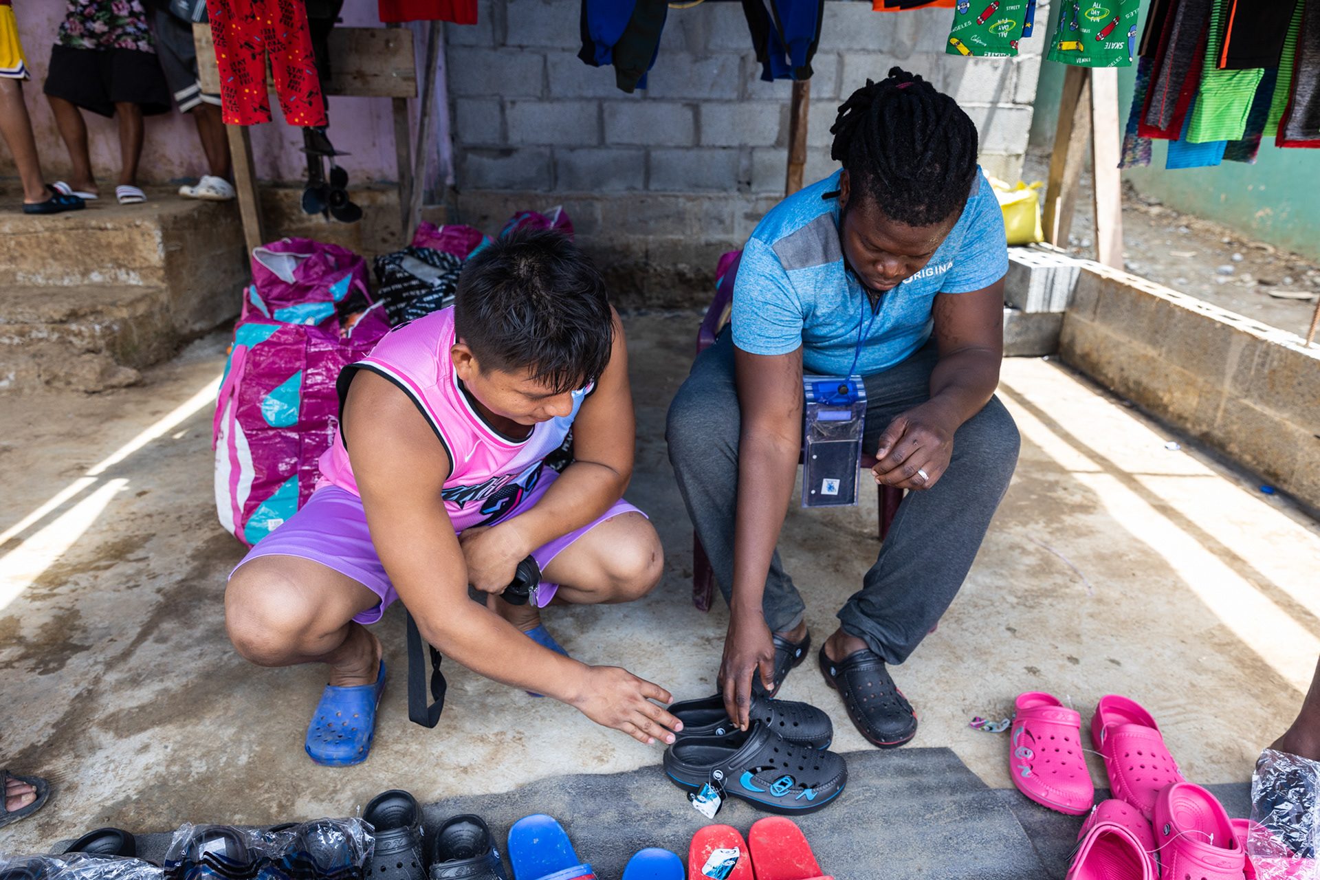 A young man in his store assists a migrant shopping for shoes.