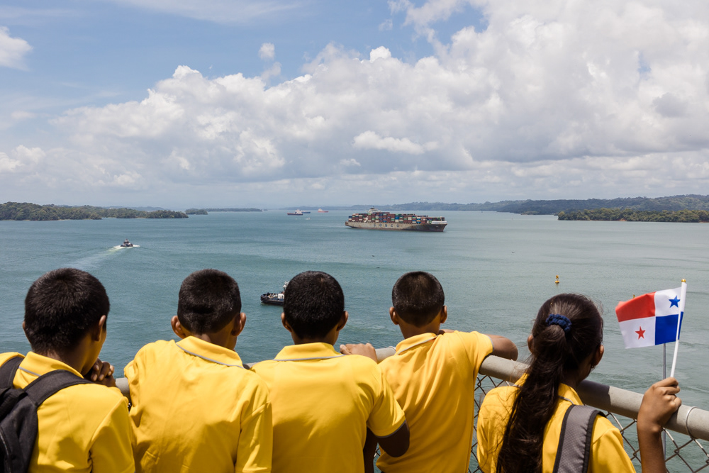 Young students watch in awe as a large ship transits Gatun Lake, viewed from the Agua Clara Locks Visitors Center. Colón, Panama. April 9, 2025.