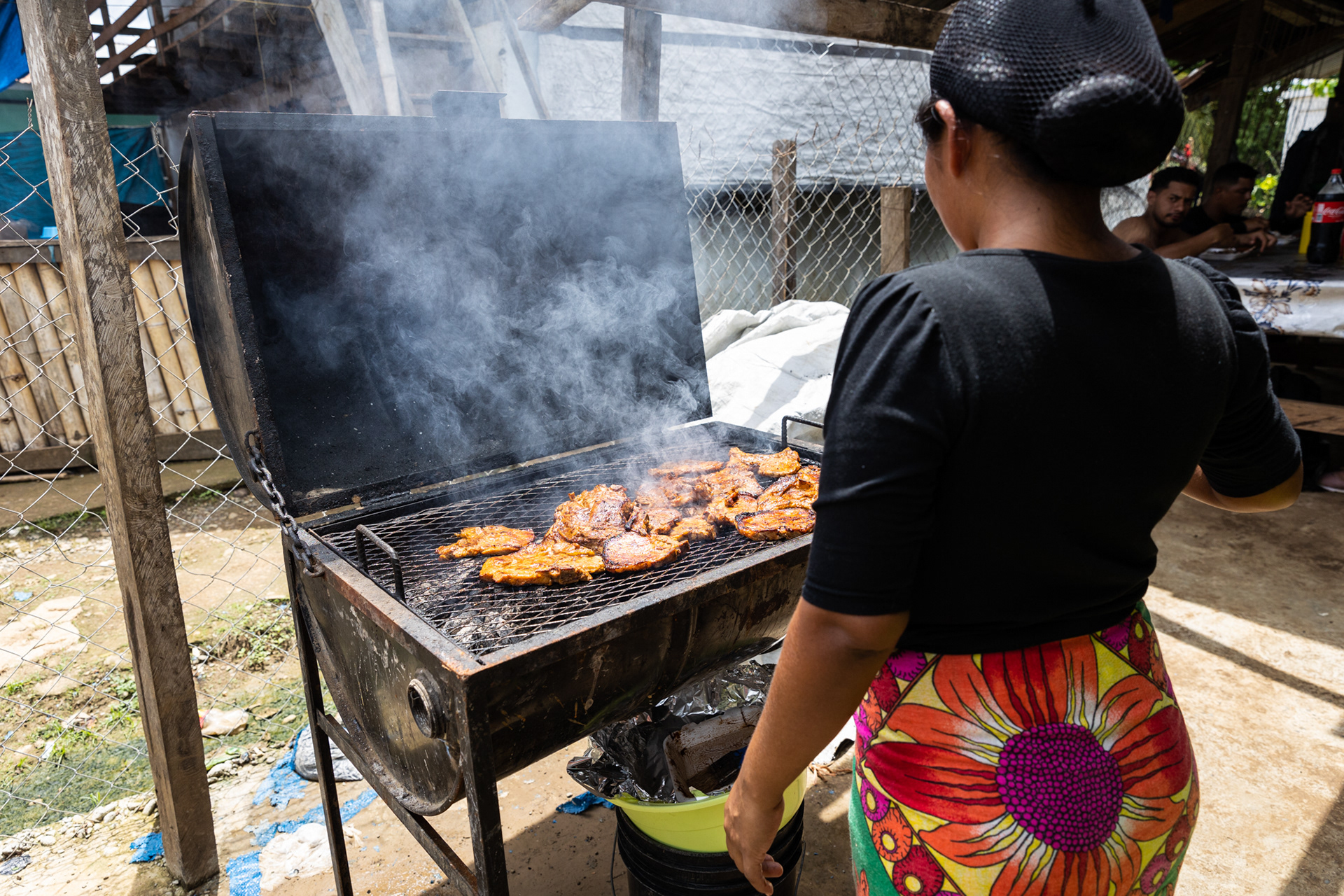 An Emberá woman grills chicken at her small restaurant, a business that sustains her family, benefiting from the passing migrants.
