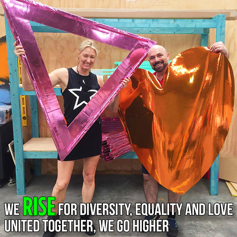 Colours of Our Community cast members Rainbow Tucker and Markham Lane hold a pink triangle and orange heart and say; united together, we go higher as we rise for diversity, equality and love in the 2021 Sydney Mardi Gras Parade. Photo by Rochelle Wallis.
