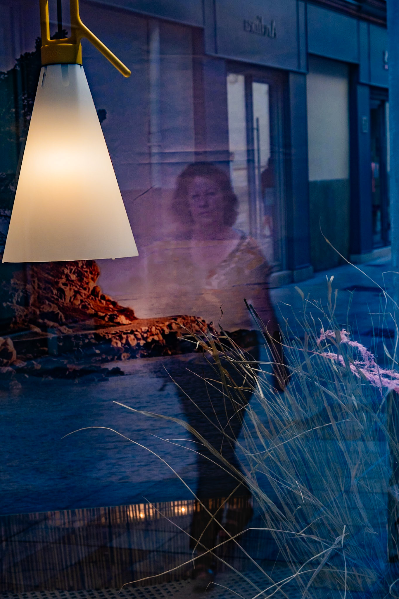 A Nimes une femme marchant dans la rue se reflète dans une vitrine abritant un décor de bord de mer.