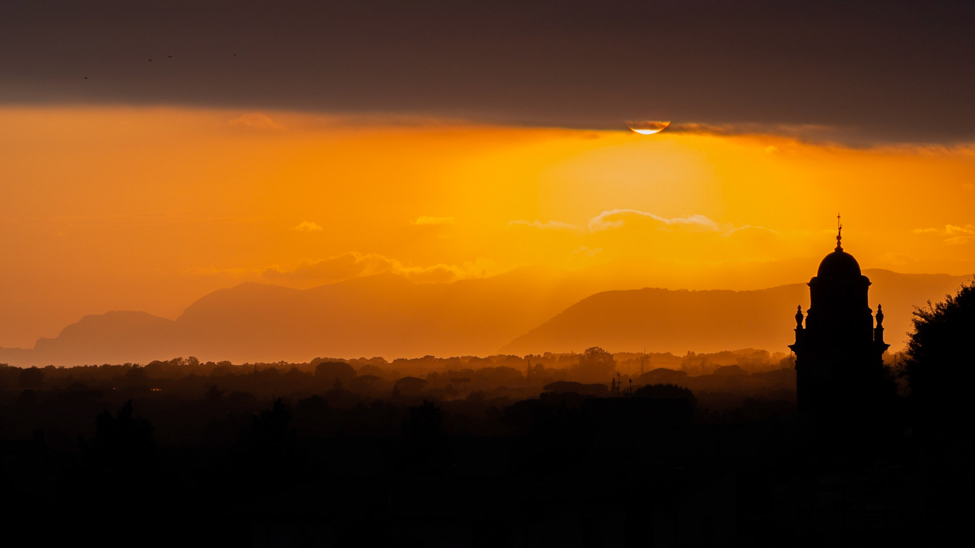 Una sera di fine luglio con il sole che tramonta dietro le colline e la silhouette del campanile di Sant'Agostino